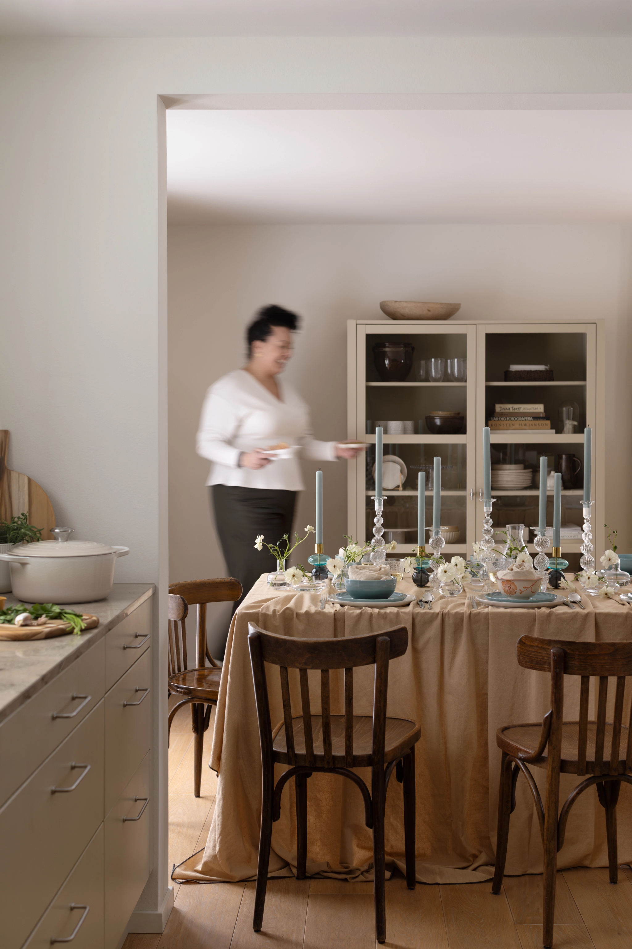 Elegant dukat matbord med blommor och höga ljus i ett ljust kök där en person serverar.