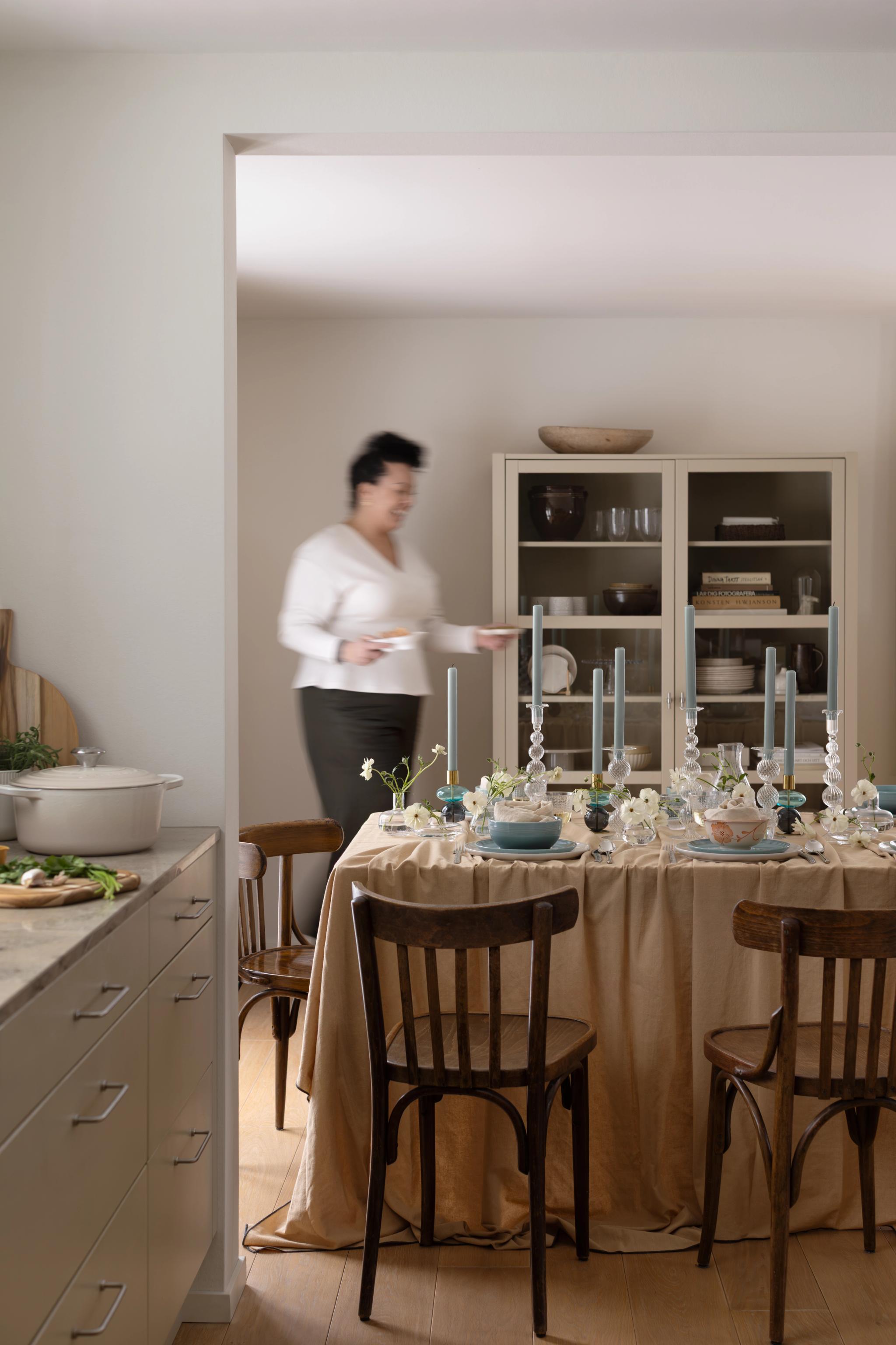 Elegant dukning med blommor och höga ljus i en ljus matsal där en kvinna serverar vid bordet.
