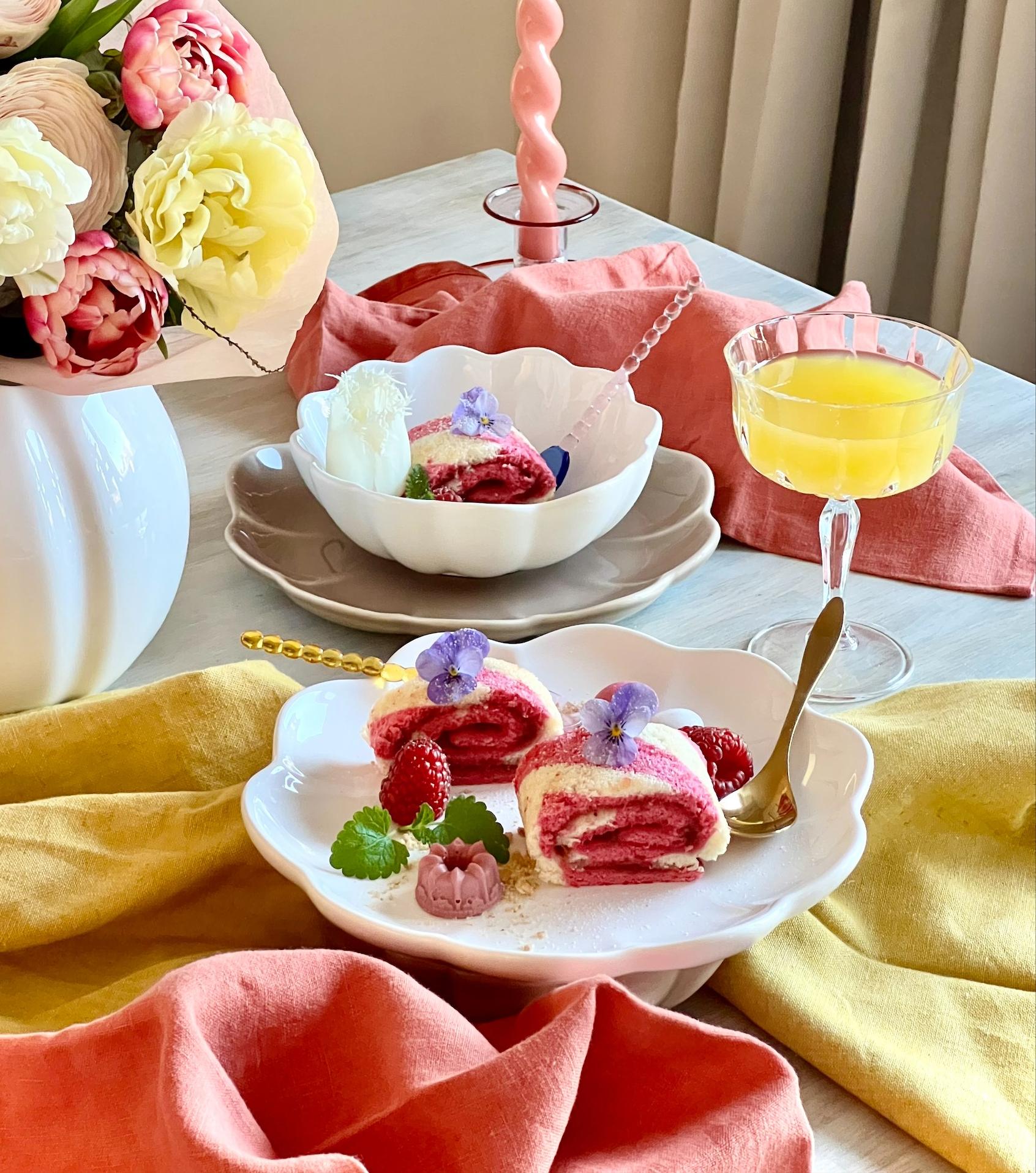 Rosa rulltårta med hallon på vit assiett