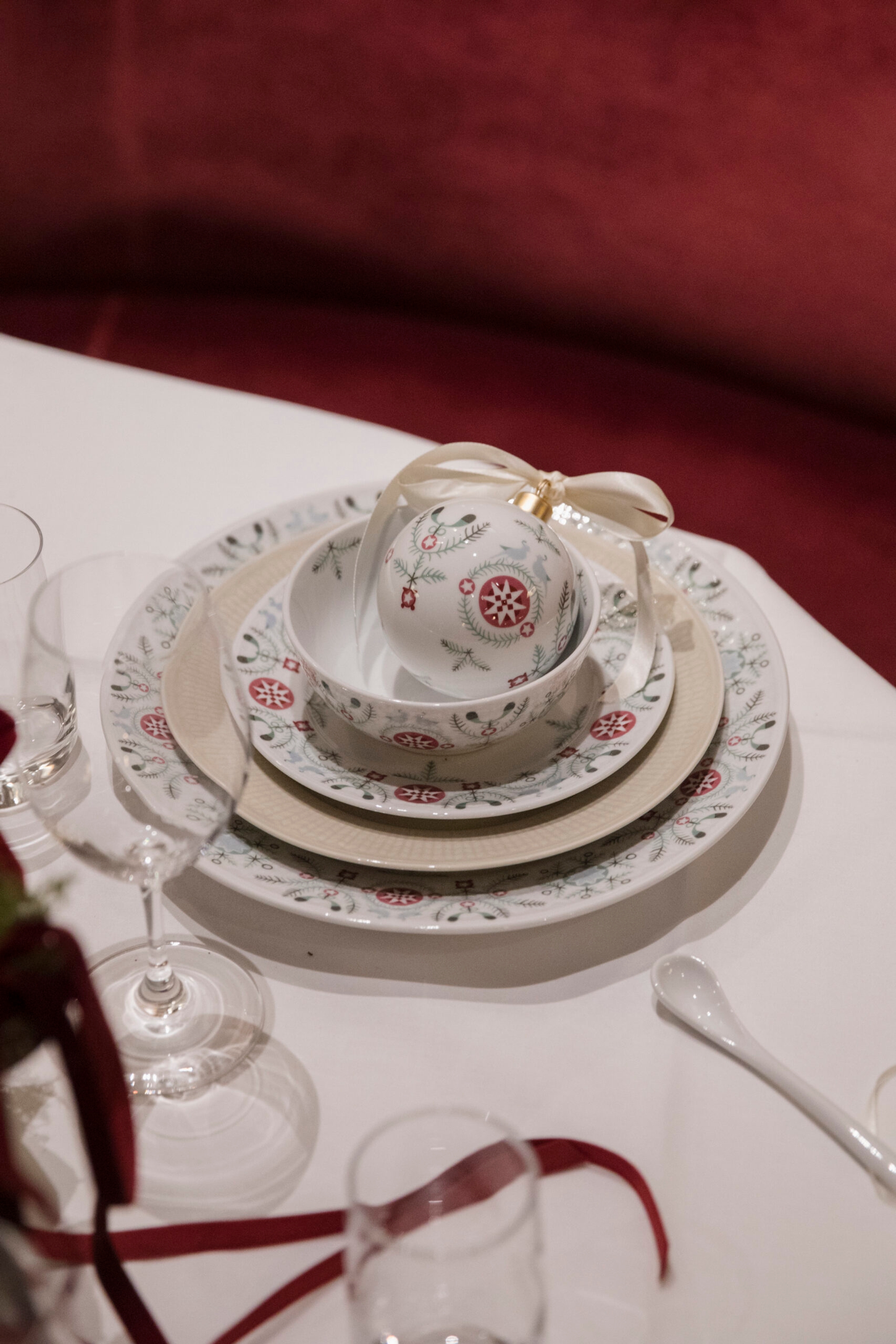 En juleborddekking med mønstrede tallerkener og en bolle, med en hvit ornament med et kremfarget bånd plassert inni bollen.