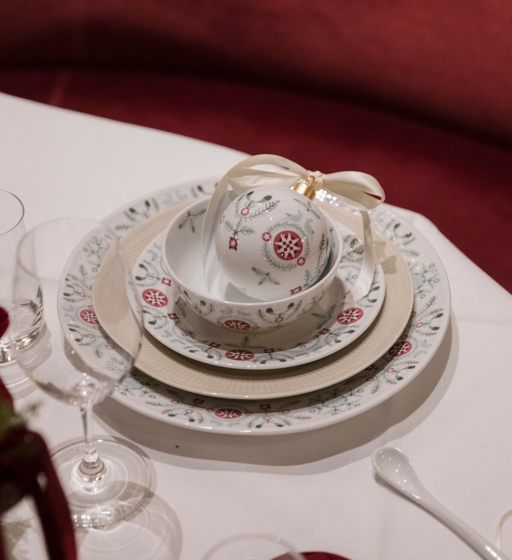 Juhlava kattaus kuviollisilla lautasilla, kulholla ja koristeellisella joulukoristeella, jossa on nauha.