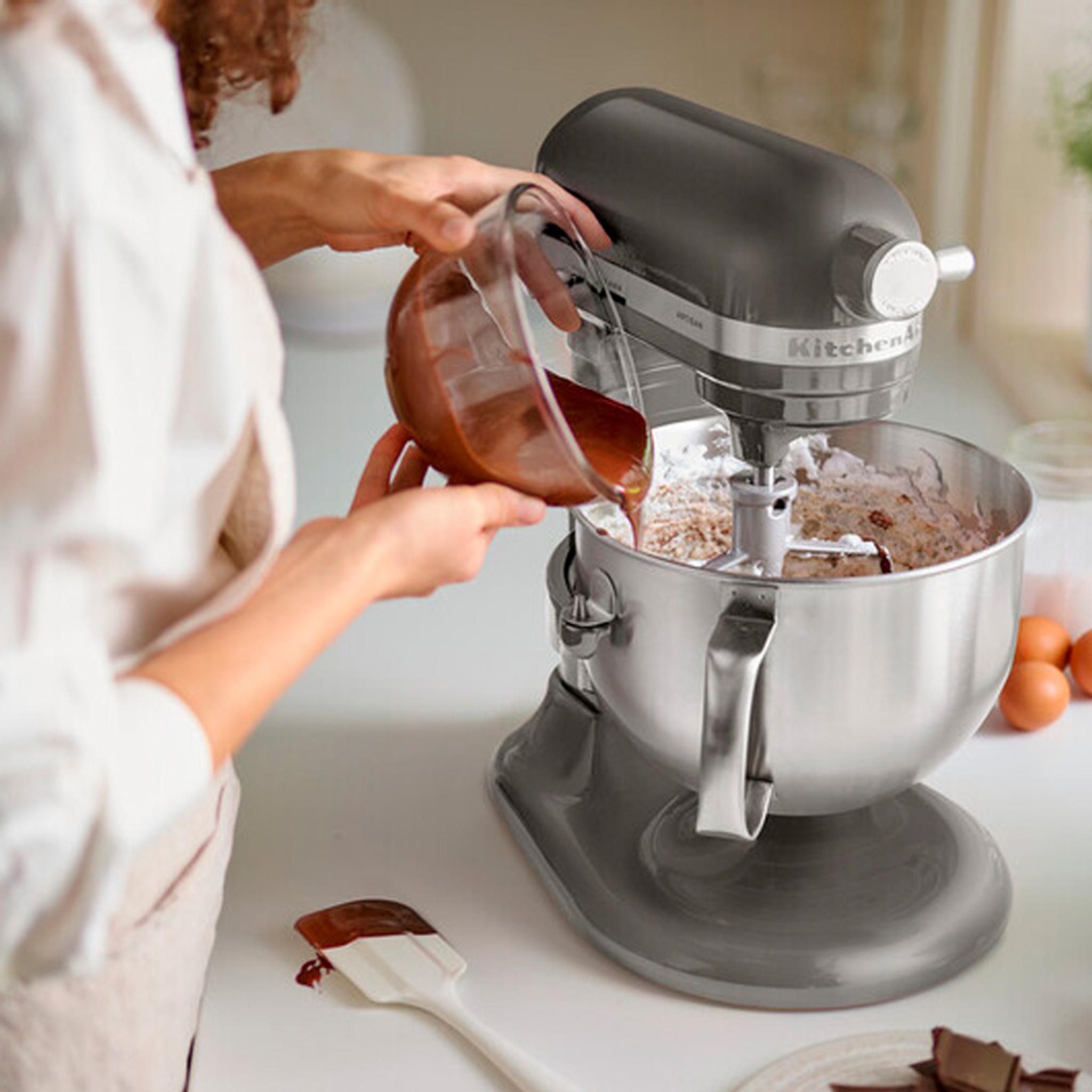 Person bakar genom att hälla smet i en stående köksmaskin av märket KitchenAid på en ljus köksbänk.