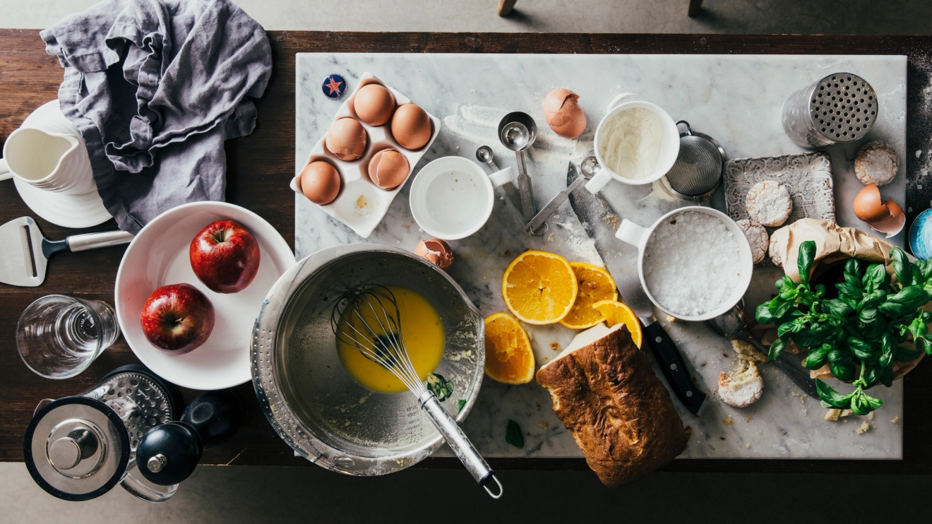 Heirol kaka som bakas på stökigt bord med ingredienser som ägg, apelsin och äpplen
