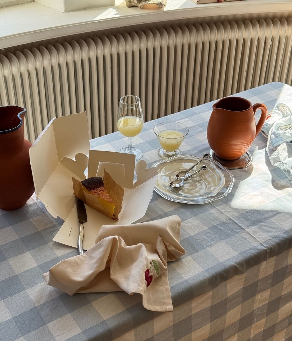 Solbelyst fikabord med rutiga dukar, keramikbringare, glas och en bit kaka.
