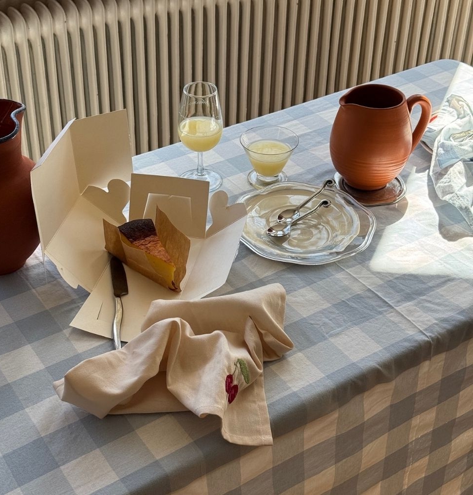 Solbelyst fikabord med rutiga dukar, keramikbringare, glas och en bit kaka.