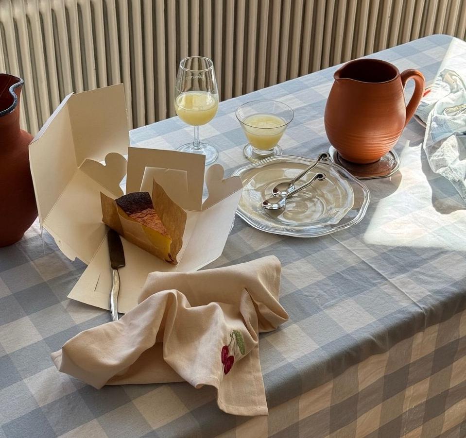 Solbelyst fikabord med rutiga dukar, keramikbringare, glas och en bit kaka.
