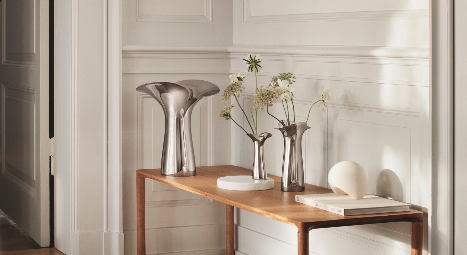 Georg Jensen vas i blankpolerat stål med skira blommor i på bord