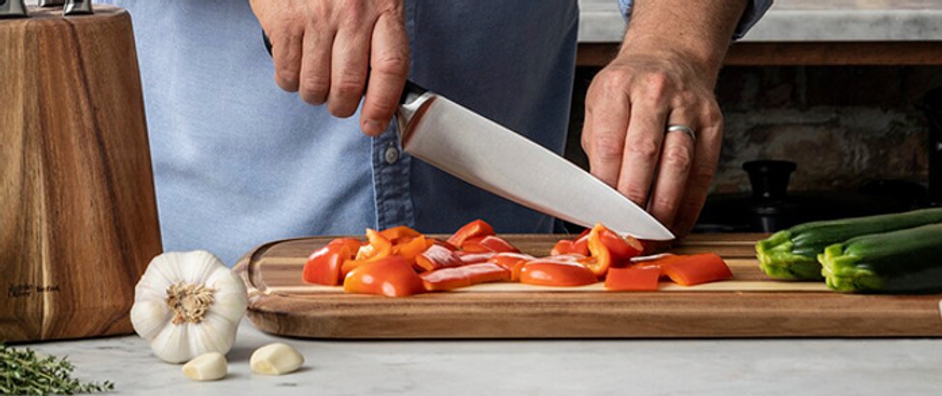 Ulike grønnsaker og en kniv som skjærer paprika