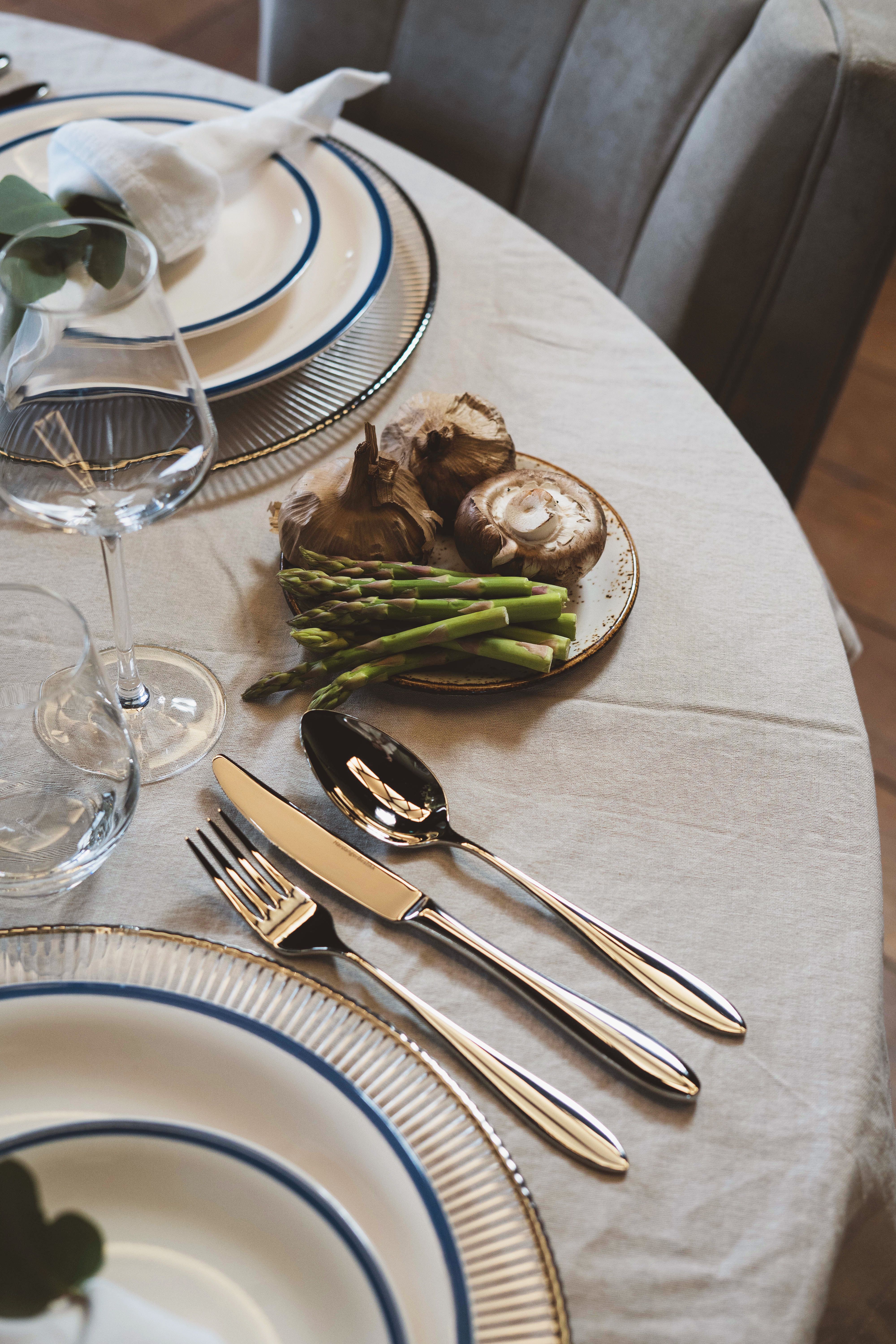 Ett matbord dukat med eleganta kuvert, bestick, ett vinglas och en liten tallrik med färsk sparris, vitlök och svamp