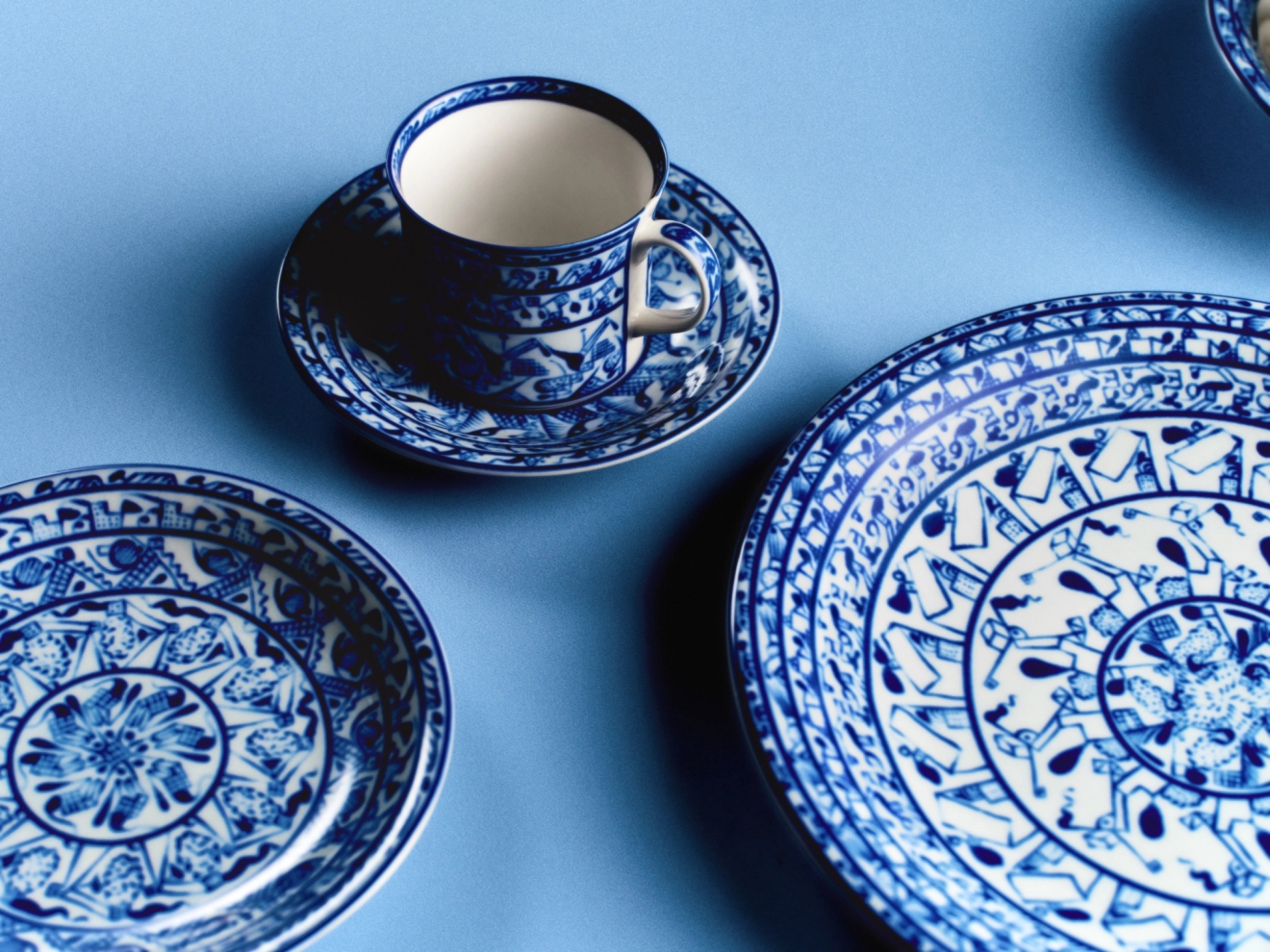 Blåvitt porslin med orientaliska mönster, inklusive tallrikar och en kaffekopp, arrangerat mot en ljusblå bakgrund.