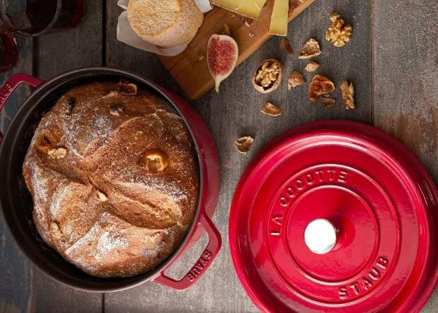 Punaisessa padassa paistettu tuore leipä tarjoillaan puupöydällä viikunoiden, juuston ja saksanpähkinöiden kanssa.