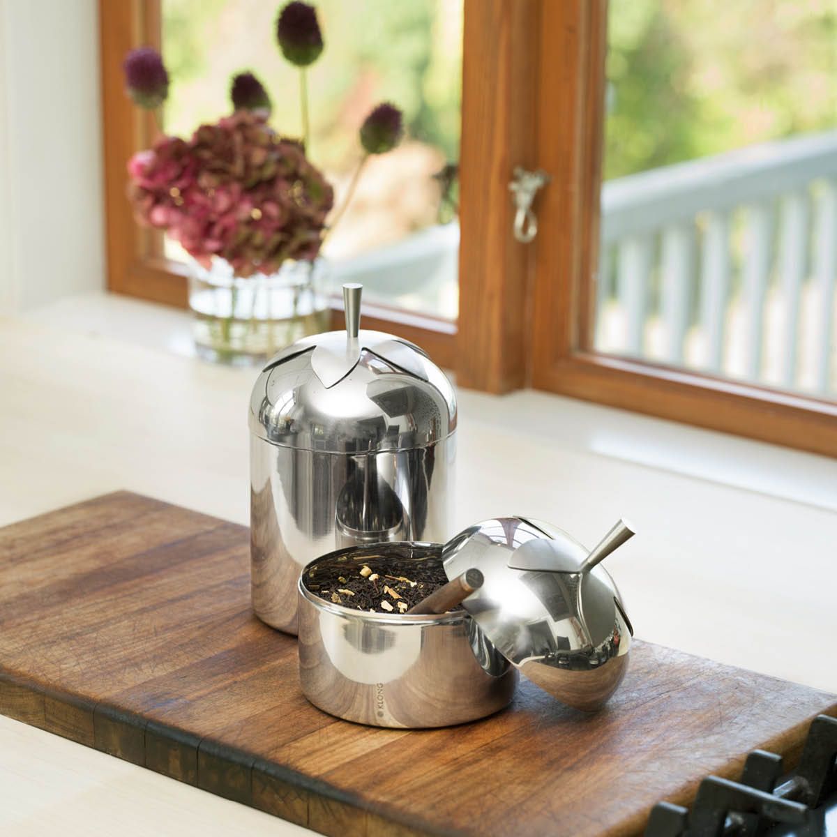 Äppelformade behållare i rostfritt stål, en öppen med lösbladigt te, på en träskiva.