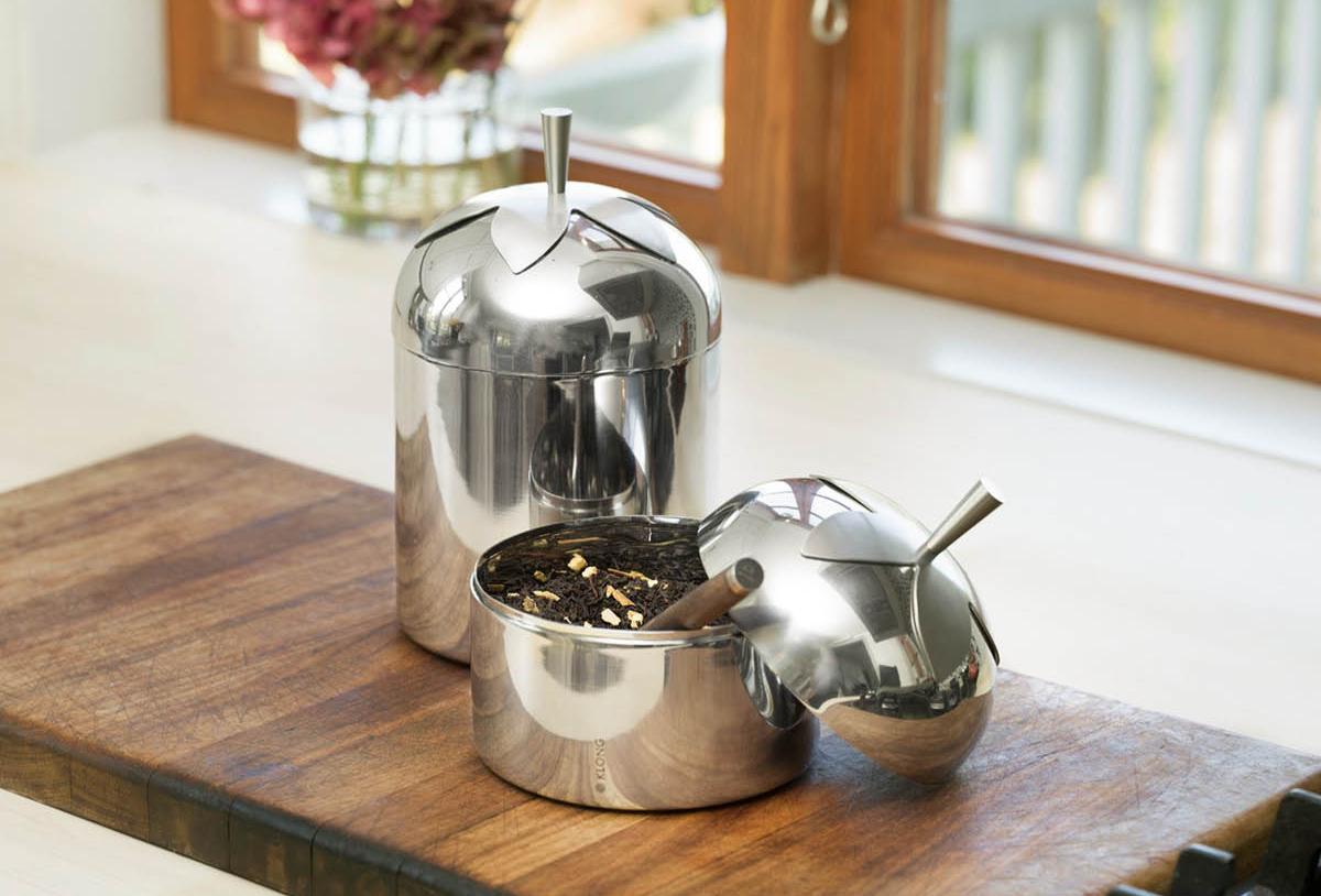 Äppelformade behållare i rostfritt stål, en öppen med lösbladigt te, på en träskiva.