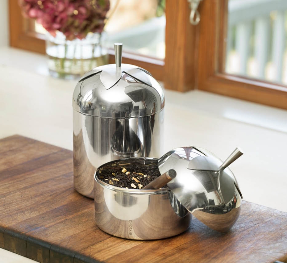 Äppelformade behållare i rostfritt stål, en öppen med lösbladigt te, på en träskiva.