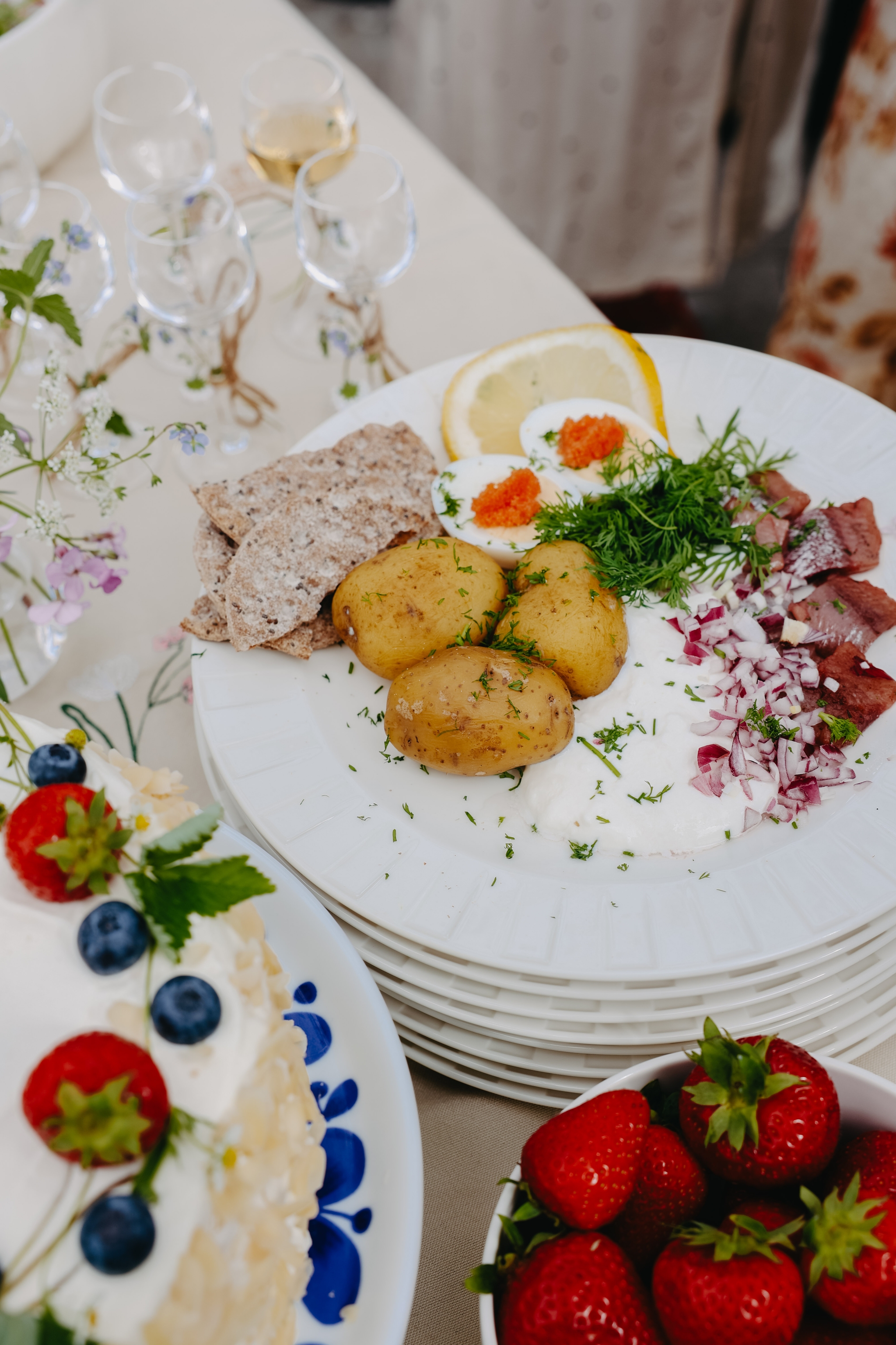Somrig svensk buffé med sill, färskpotatis, ägg med rom, knäckebröd, jordgubbar och gräddtårta med bär.