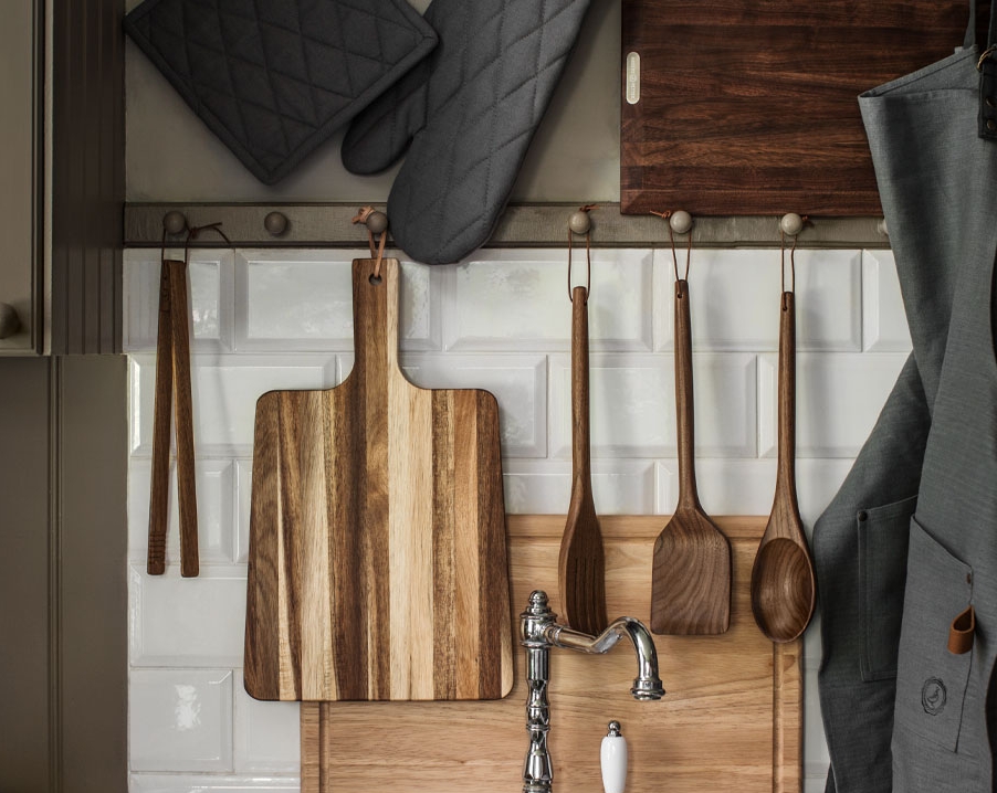 Puiset keittiövälineet - kauha, paistinlasta, pihdit ja leikkuulauta roikkuu seinällä