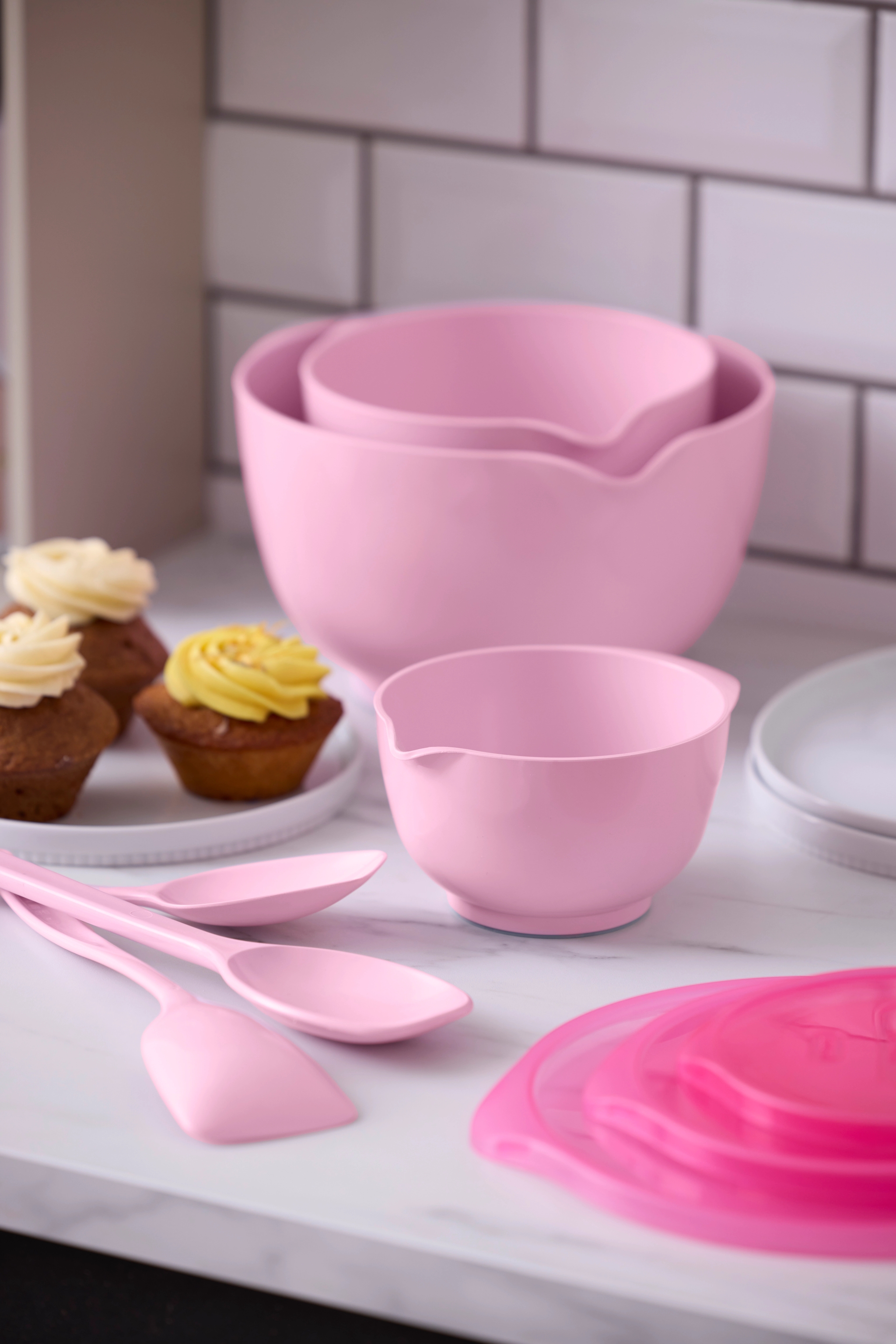 Rosa bakskålar och köksredskap står bredvid nybakade muffins med färgglad frosting.