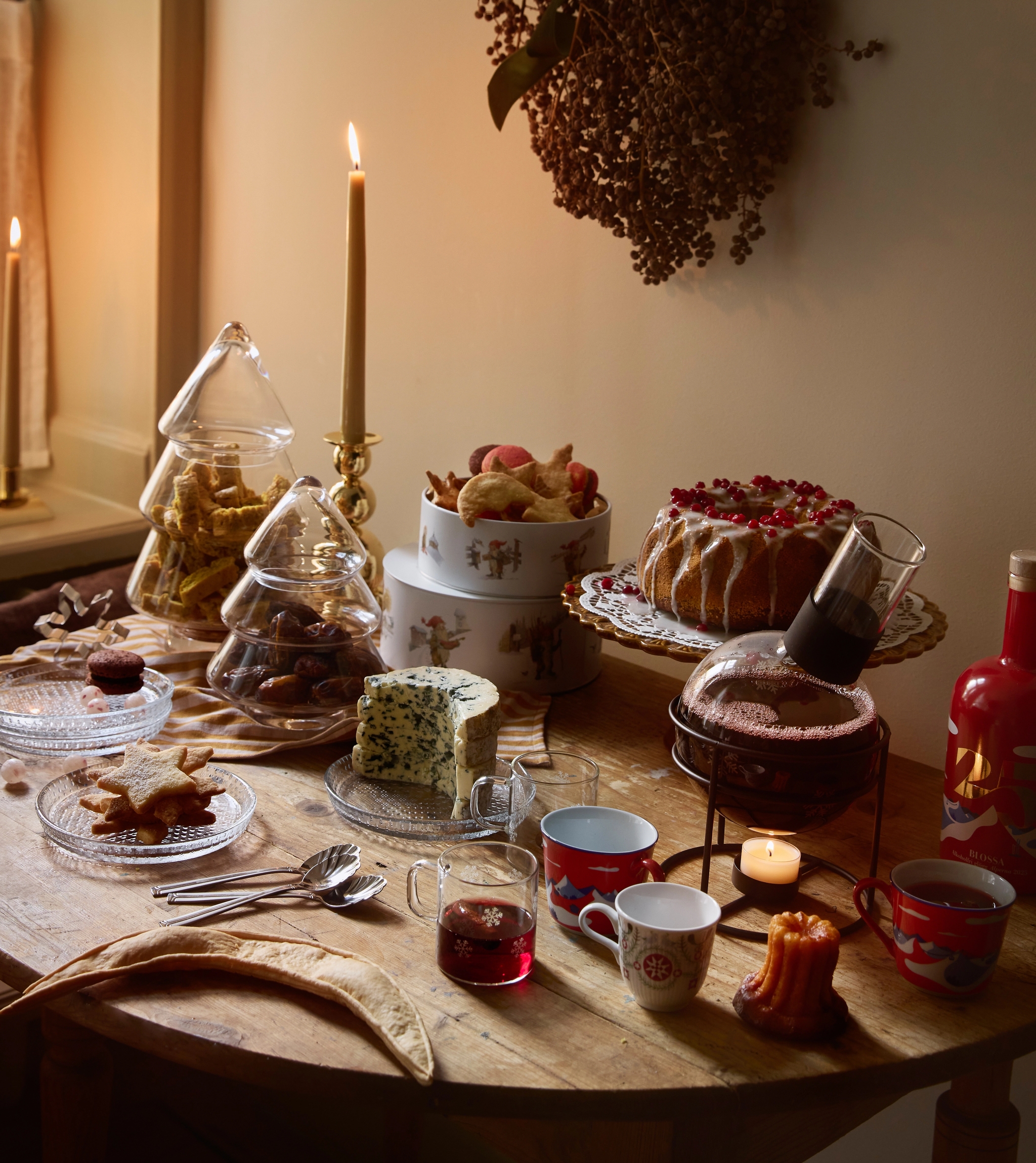 Juhlava, kynttilänvalossa loistava pöytä, joka on katettu naposteltavilla, jälkiruoilla ja juomilla ikkunan vieressä.