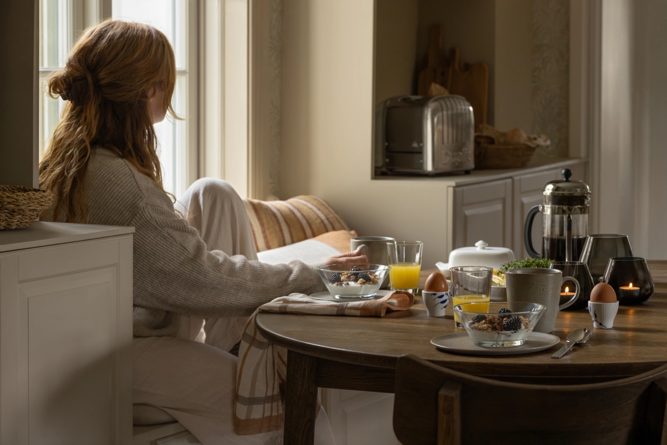 En kvinne sitter ved et bord og spiser frokost mens hun leser en bok