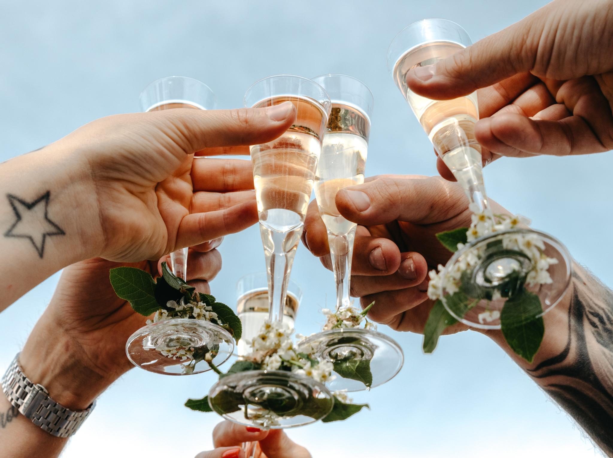 Flera händer skålar med champagneglas dekorerade med blommor mot en blå himmel.