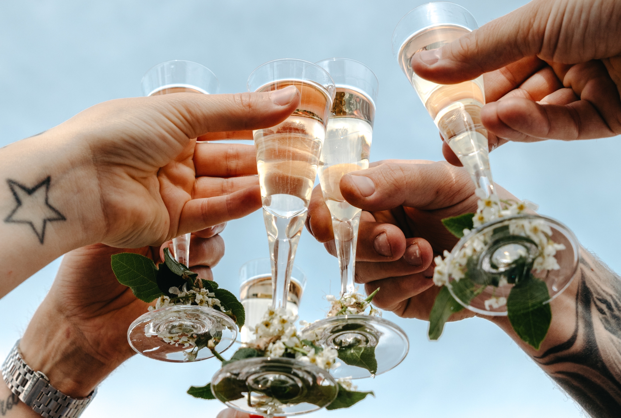 Flera händer skålar med champagneglas dekorerade med blommor mot en blå himmel.