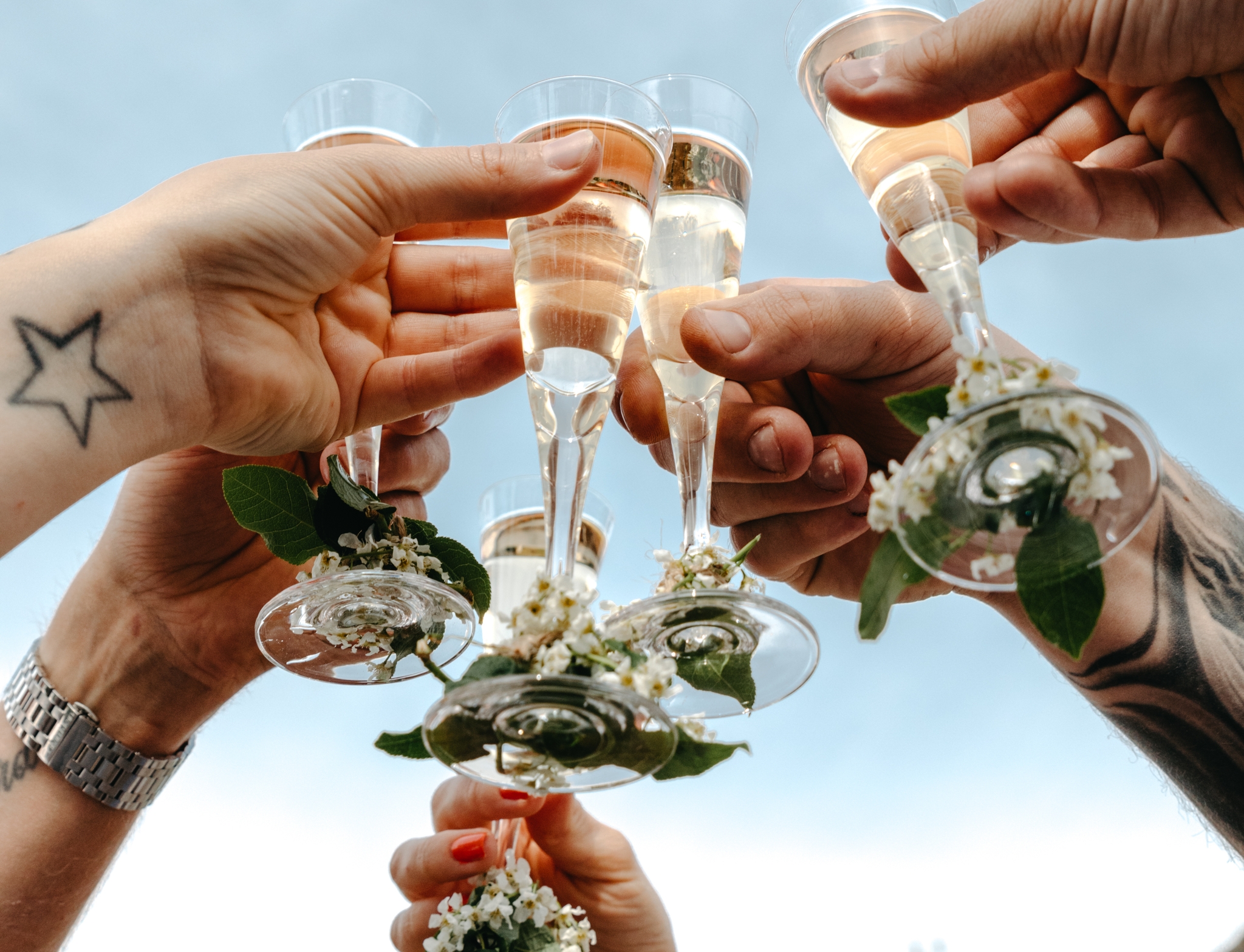Venner skåler med champagneglass pyntet med blomster under åpen himmel.
