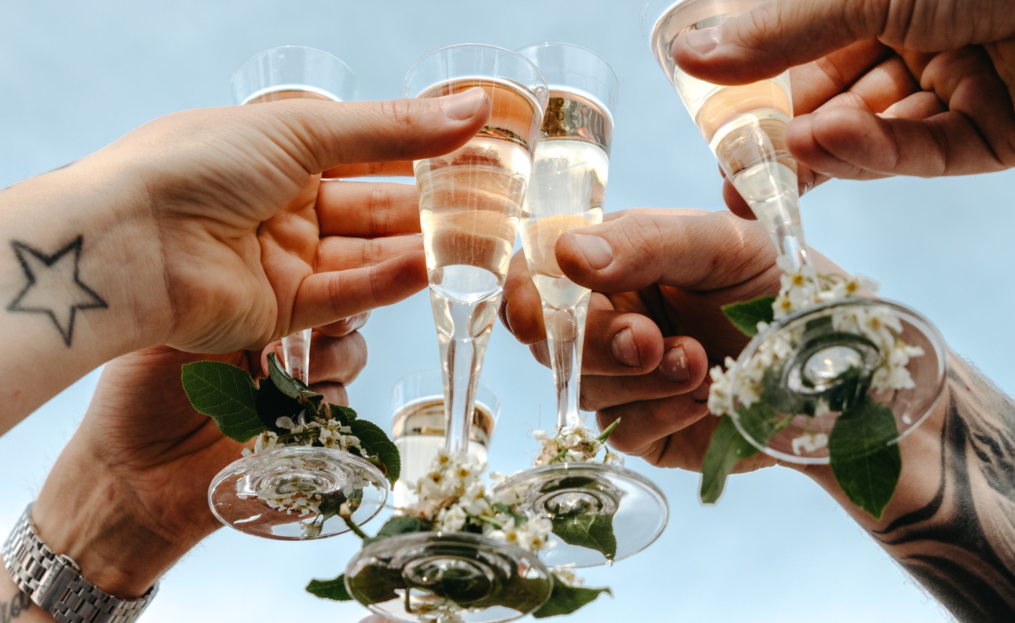 Flera händer skålar med champagneglas dekorerade med blommor mot en blå himmel.