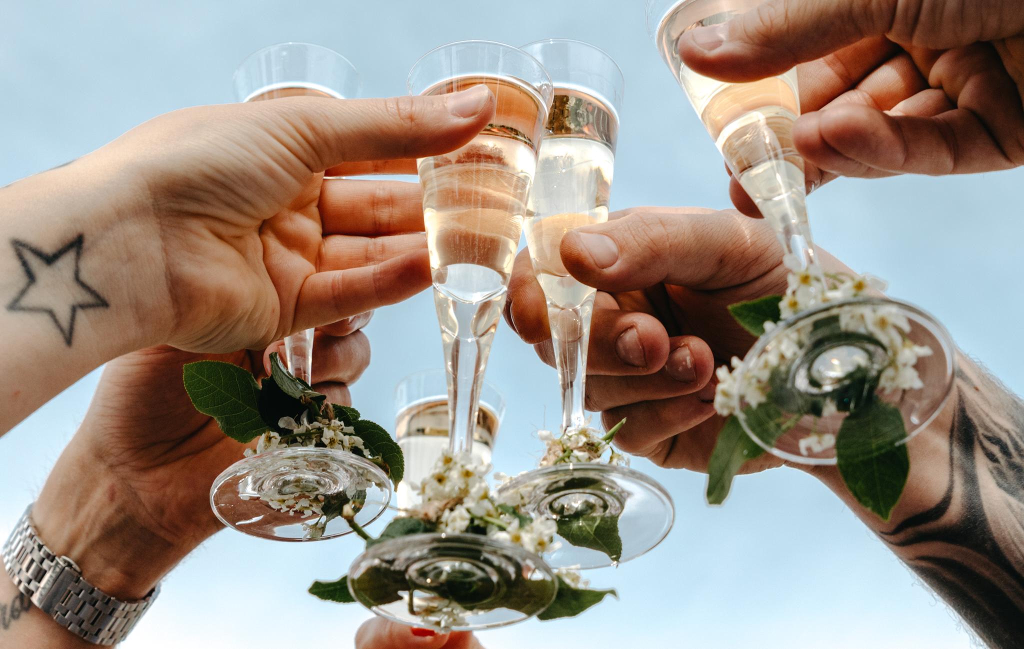 Flera händer höjer champagneglas dekorerade med blommor mot himlen i en festlig skål.