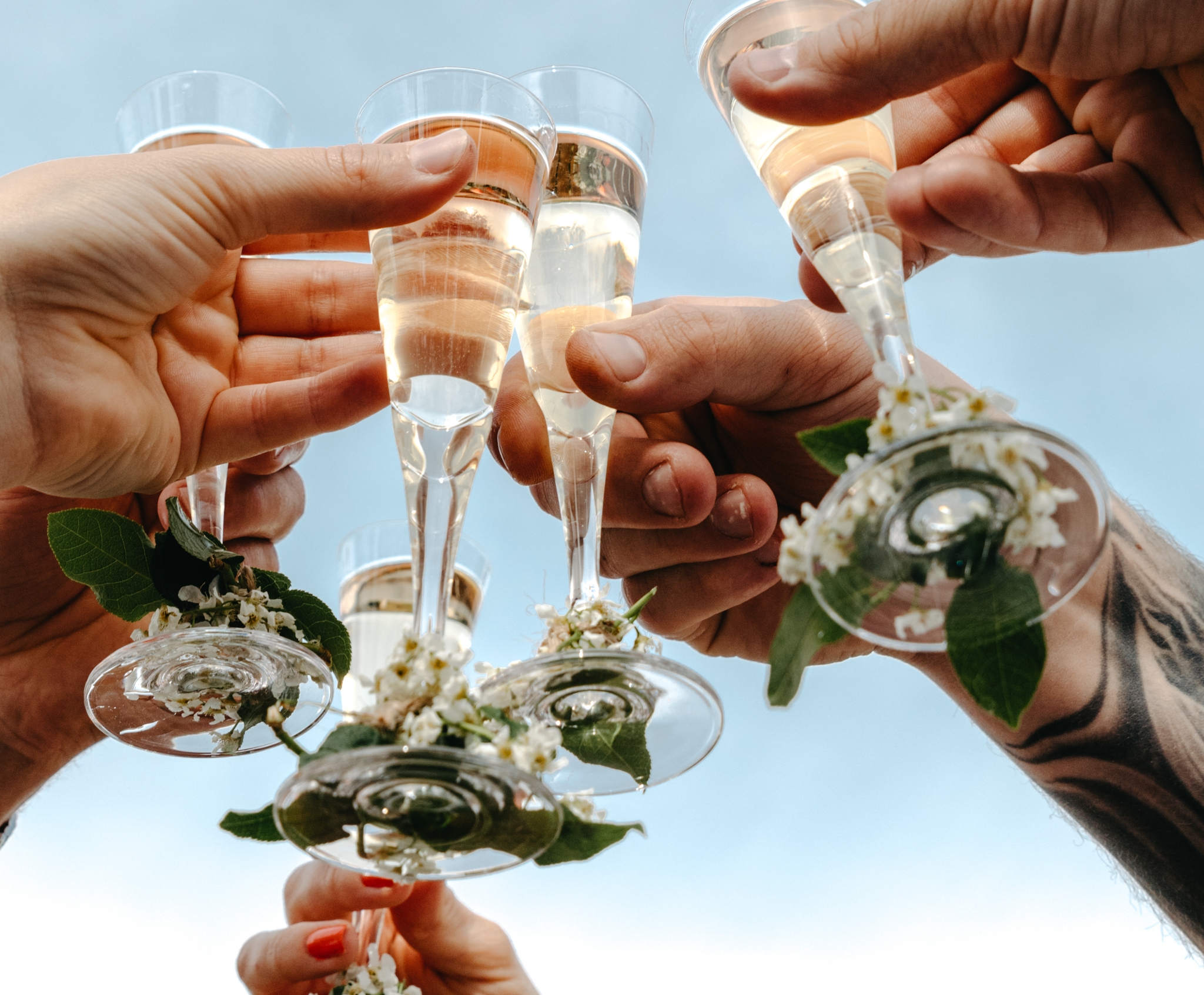 Flera händer skålar med champagneglas dekorerade med blommor mot en blå himmel.
