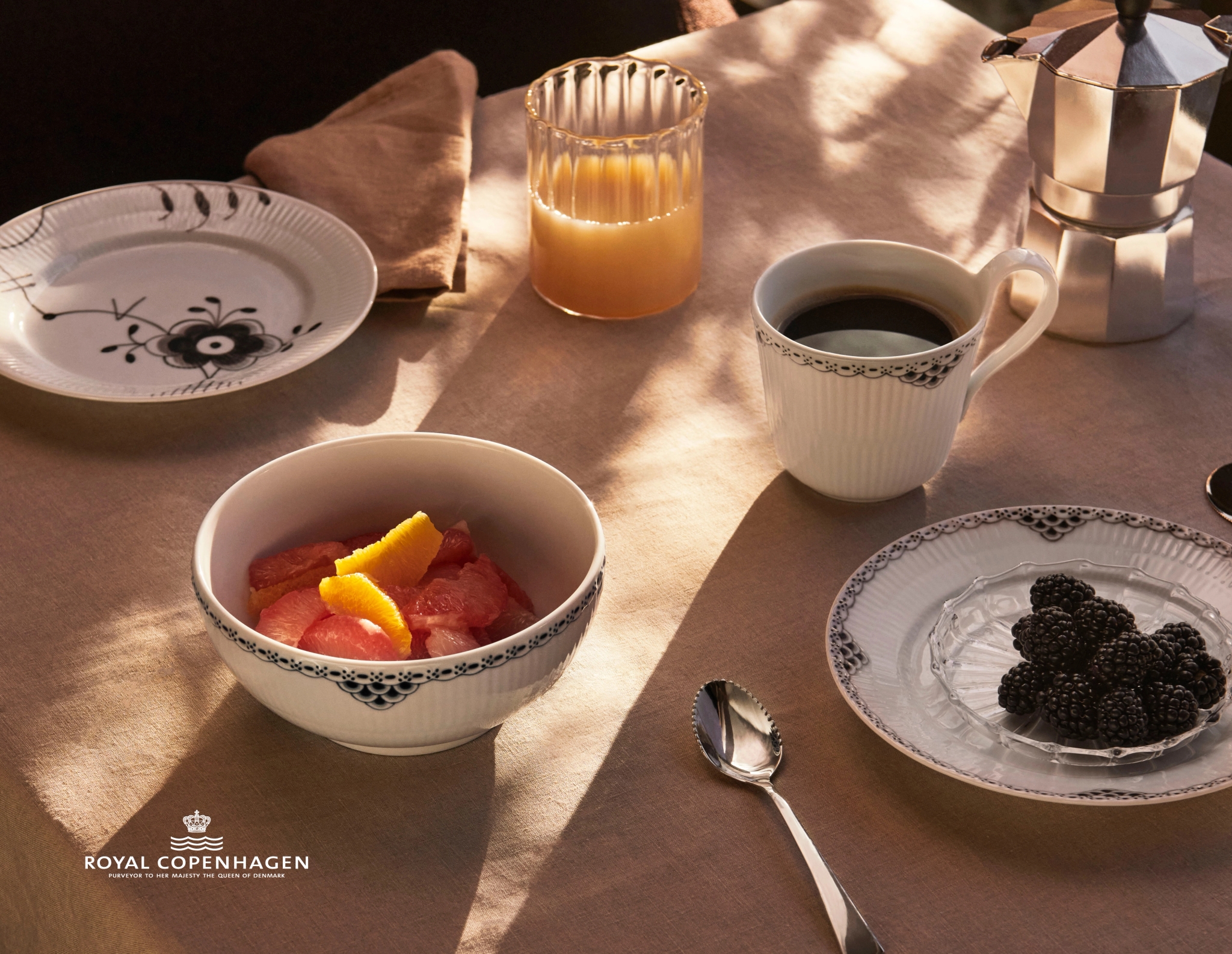 Ett solbelyst frukostbord dukat med porslin från Royal Copenhagen, inklusive kaffe, apelsinjuice, en fruktskål och björnbär.