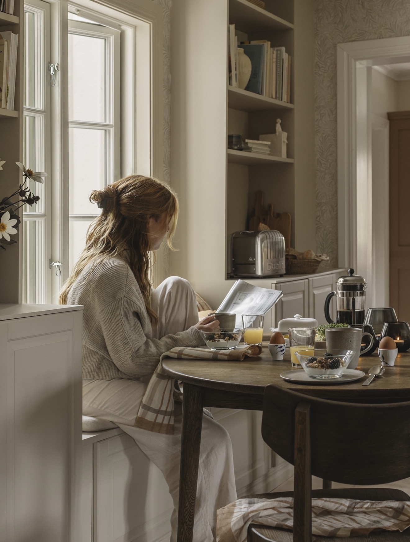 En kvinne sitter ved et bord og leser et magasin