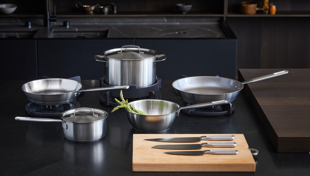 Uppsättning rostfria kastruller, stekpannor och köksknivar på en modern svart köksbänk.