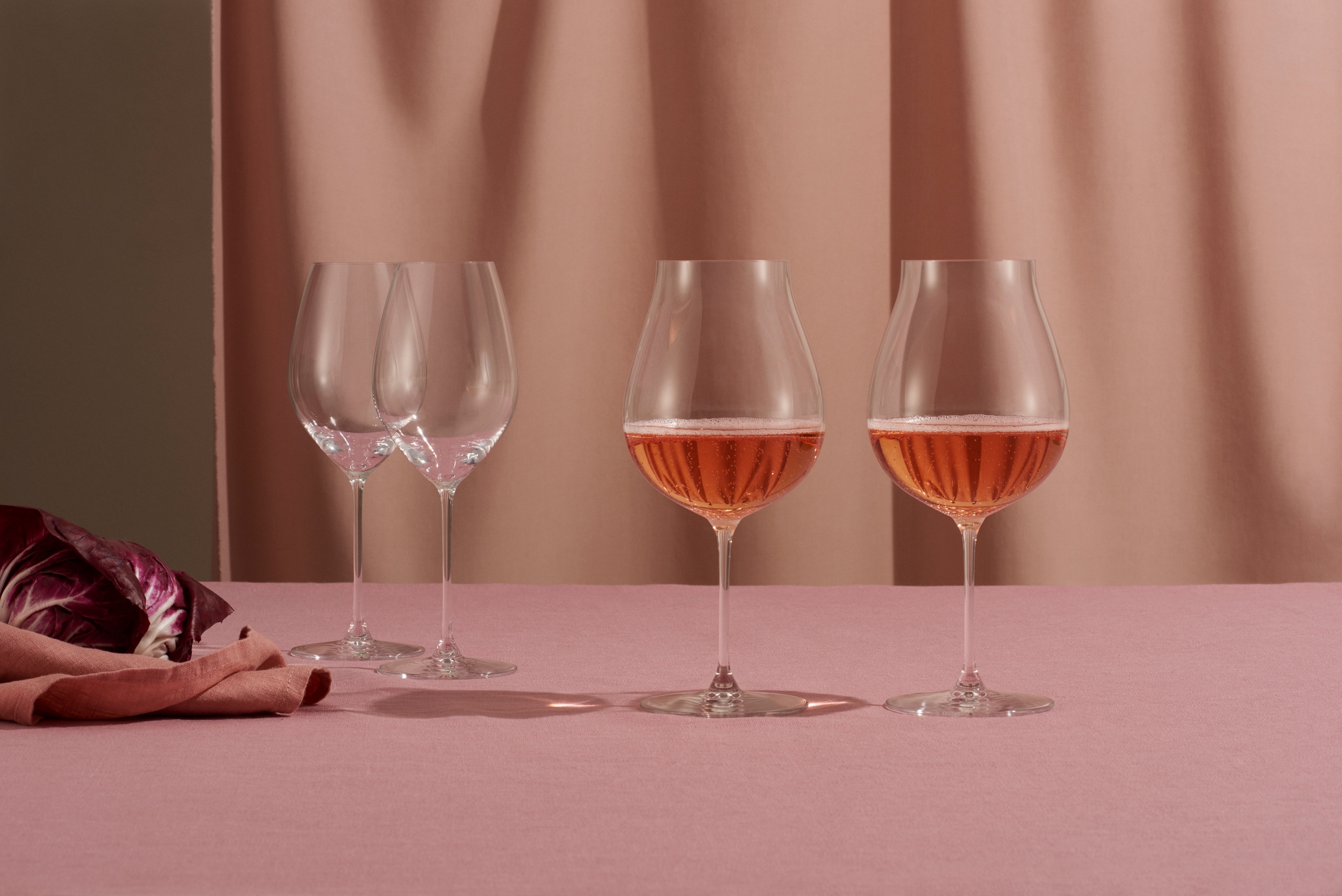 Fyra vinglas på ett rosa bord, två tomma och två fyllda med rosé.