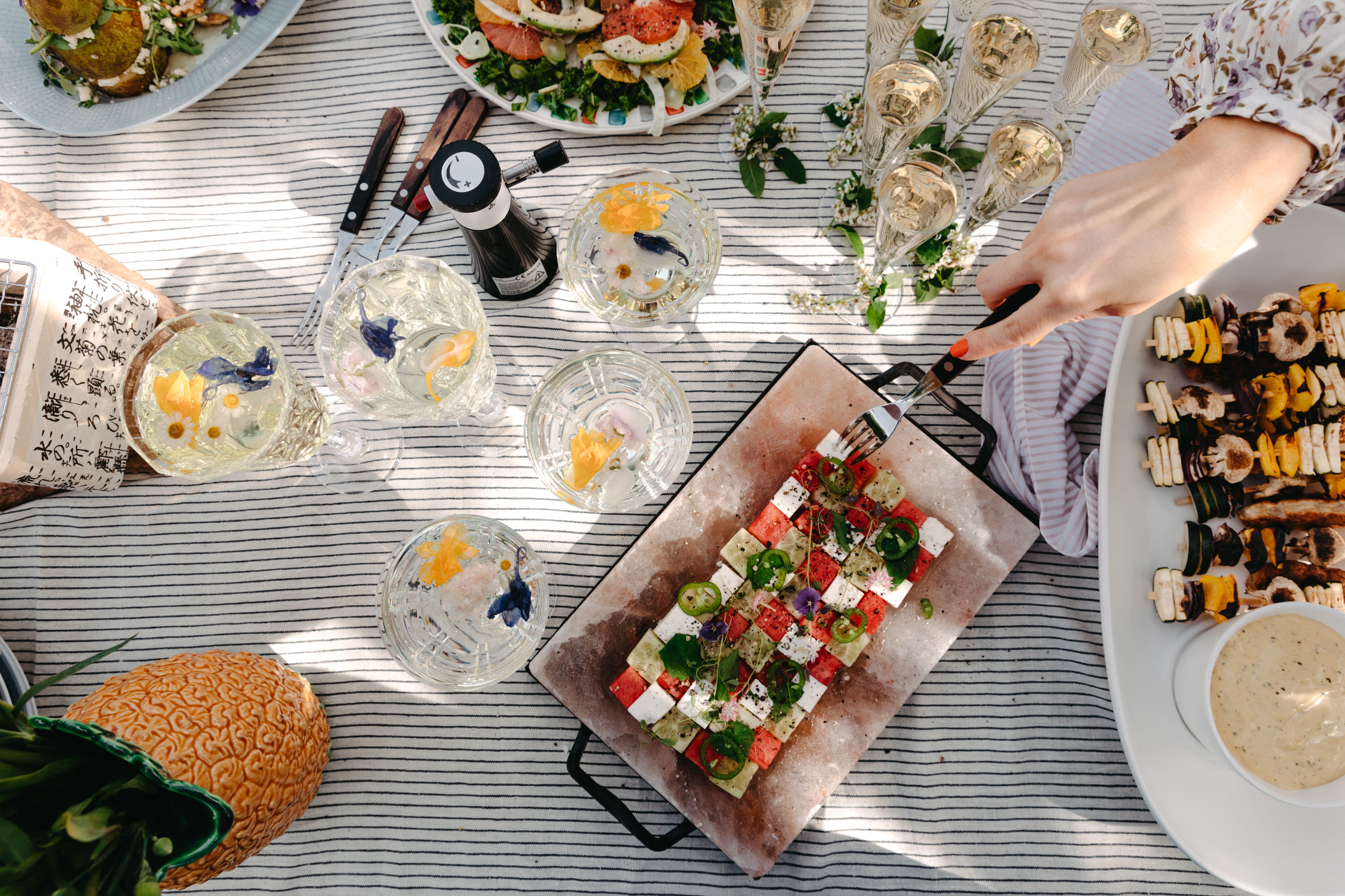 Sommerlig piknikbord med fargerik salat, grillspyd, bobler og drinker pyntet med spiselige blomster.