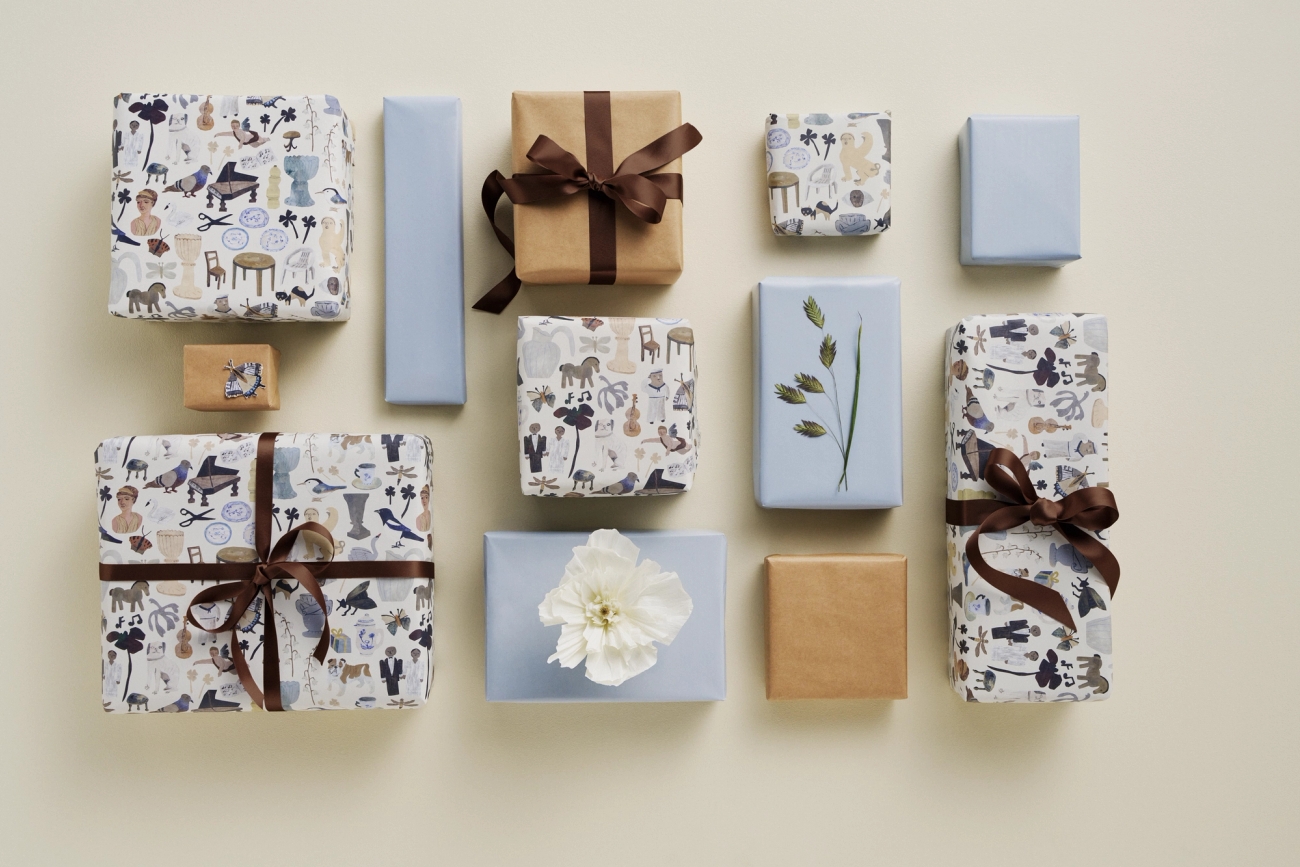Vackert inslagna paket i ljusblätt och beige presentpapper med dekorativa blommor och snören