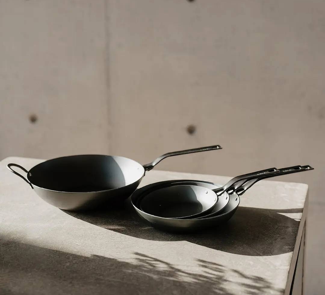 Heirol hiiliteräspannut blacksteel sarjasta pinottu päällekkäin vaalealla pöydällä betoniseinää vasten.