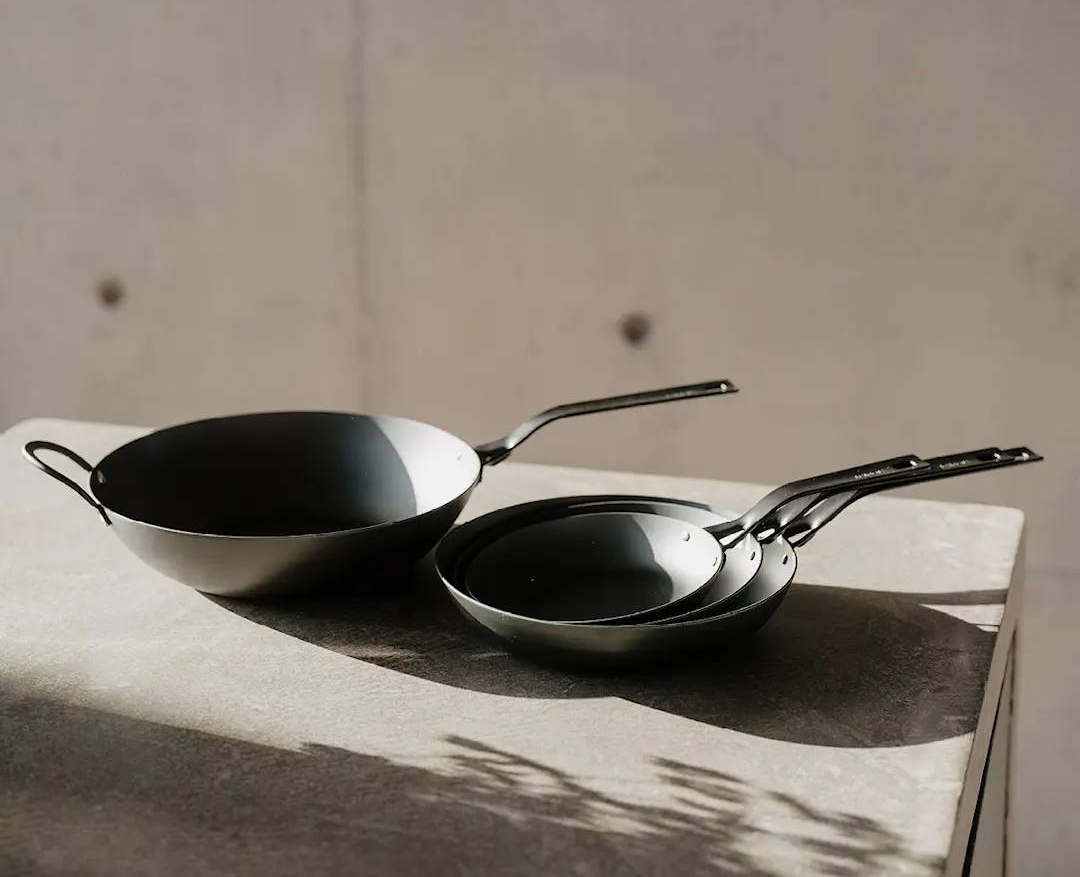 Heirol hiiliteräspannut blacksteel sarjasta pinottu päällekkäin vaalealla pöydällä betoniseinää vasten.