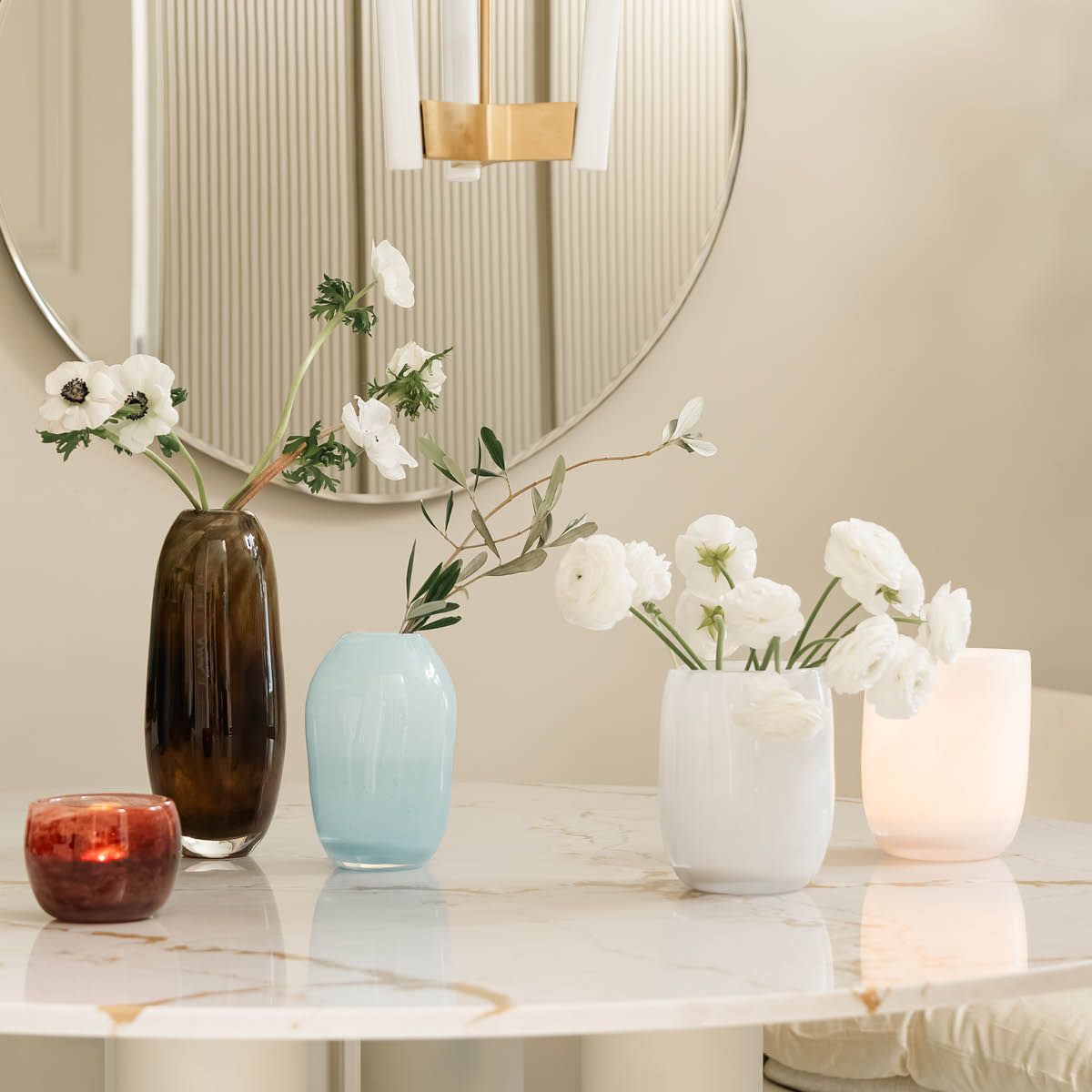 Dekorative glassvaser med blomster og et glødende lys på et marmorbord.