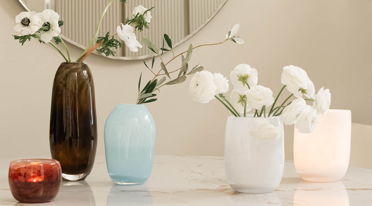 Dekorative glassvaser med blomster og et glødende lys på et marmorbord.