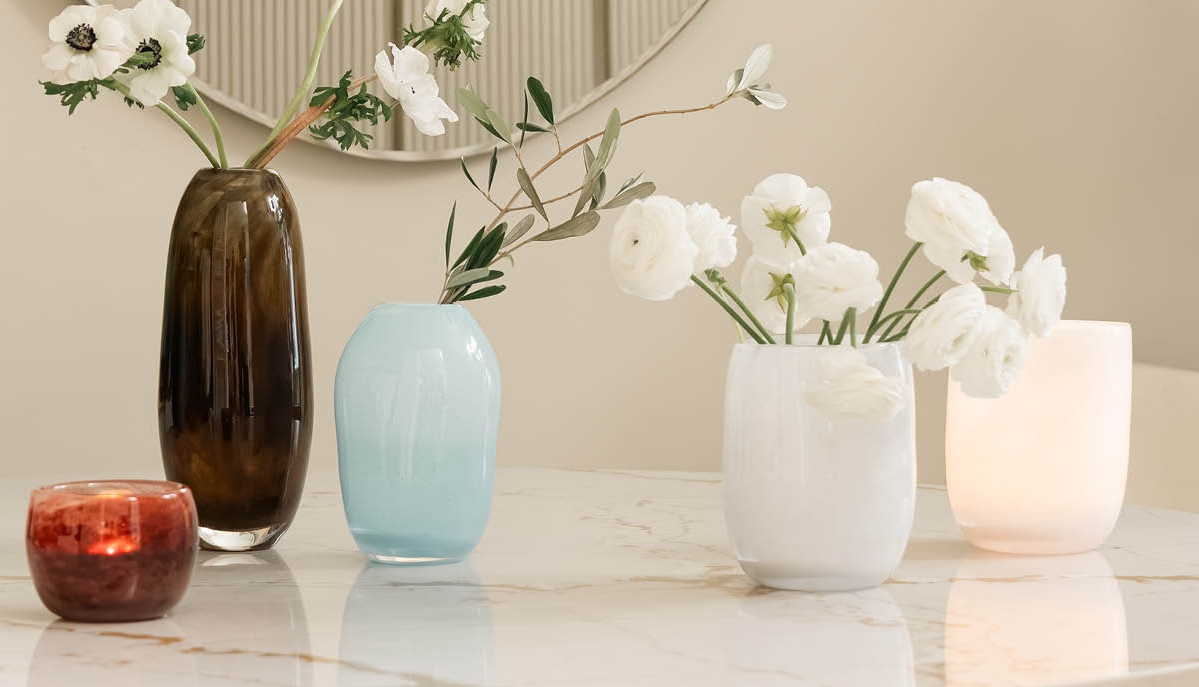 Dekorative glassvaser med blomster og et glødende lys på et marmorbord.