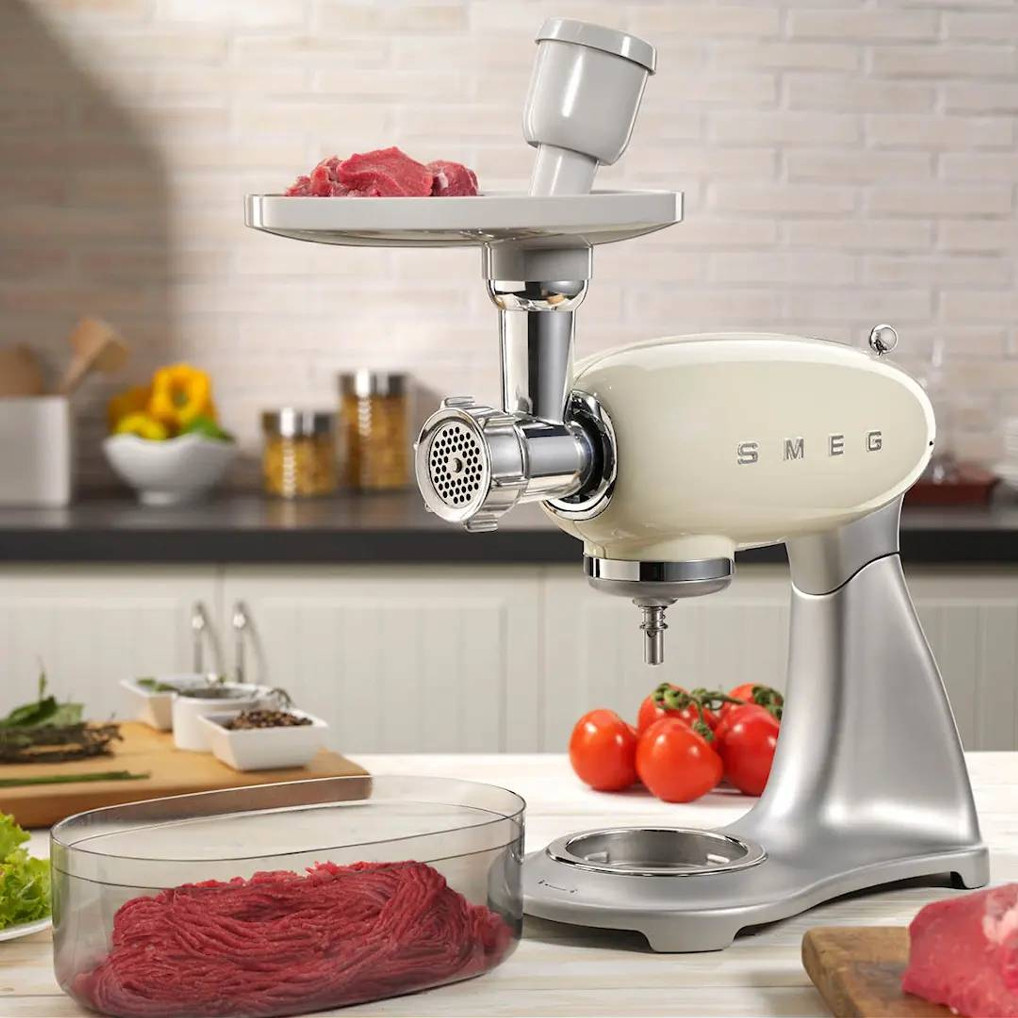 Smeg köttkvarn i krämfärg på köksbänk maler färskt kött med grönsaker i bakgrunden.