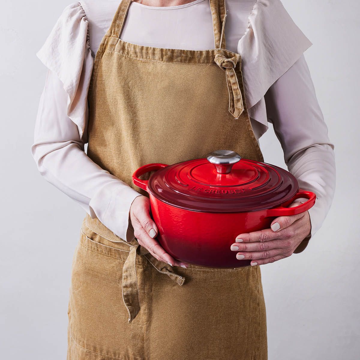 Person i forkle holder en rød Le Creuset-gryte med lokk.