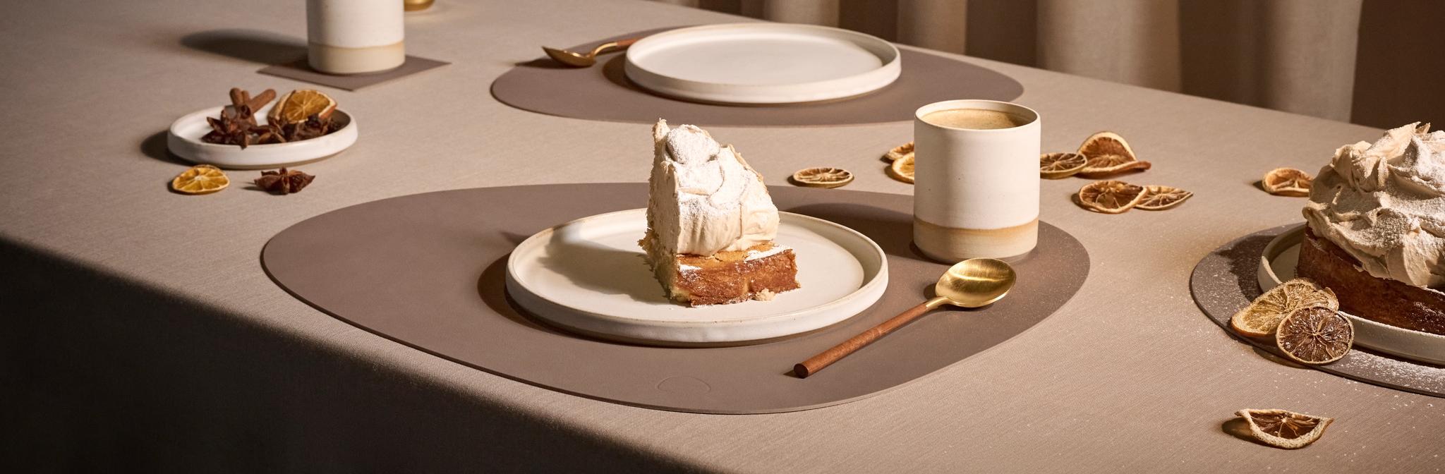 Stilrent dukat bord med bit citronmarängpaj, tända ljus och torkade citrusfrukter i varm, beige miljö.