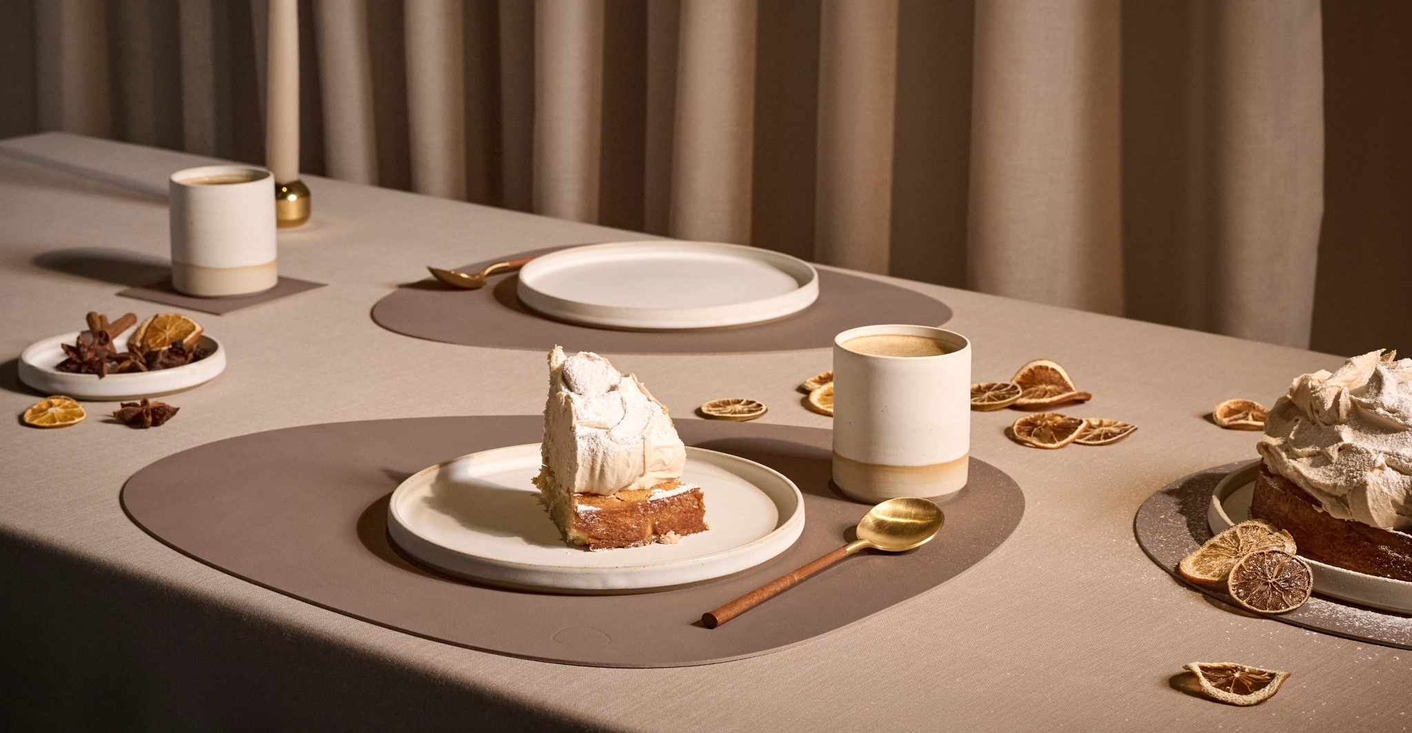 Stilrent dukat bord med tårta, kaffe, tända ljus och torkade citronskivor i varm, beige miljö.