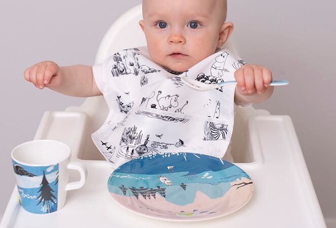 Rätt Start bebis sitter i barnstol med haklapp, tallrik, mugg och sked