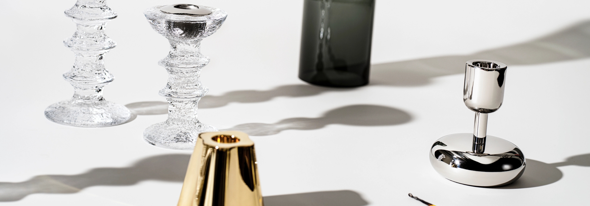 Modernit lasi- ja metallikynttilänjalat aseteltuna valkoiselle taustalle design-sisustusta varten.