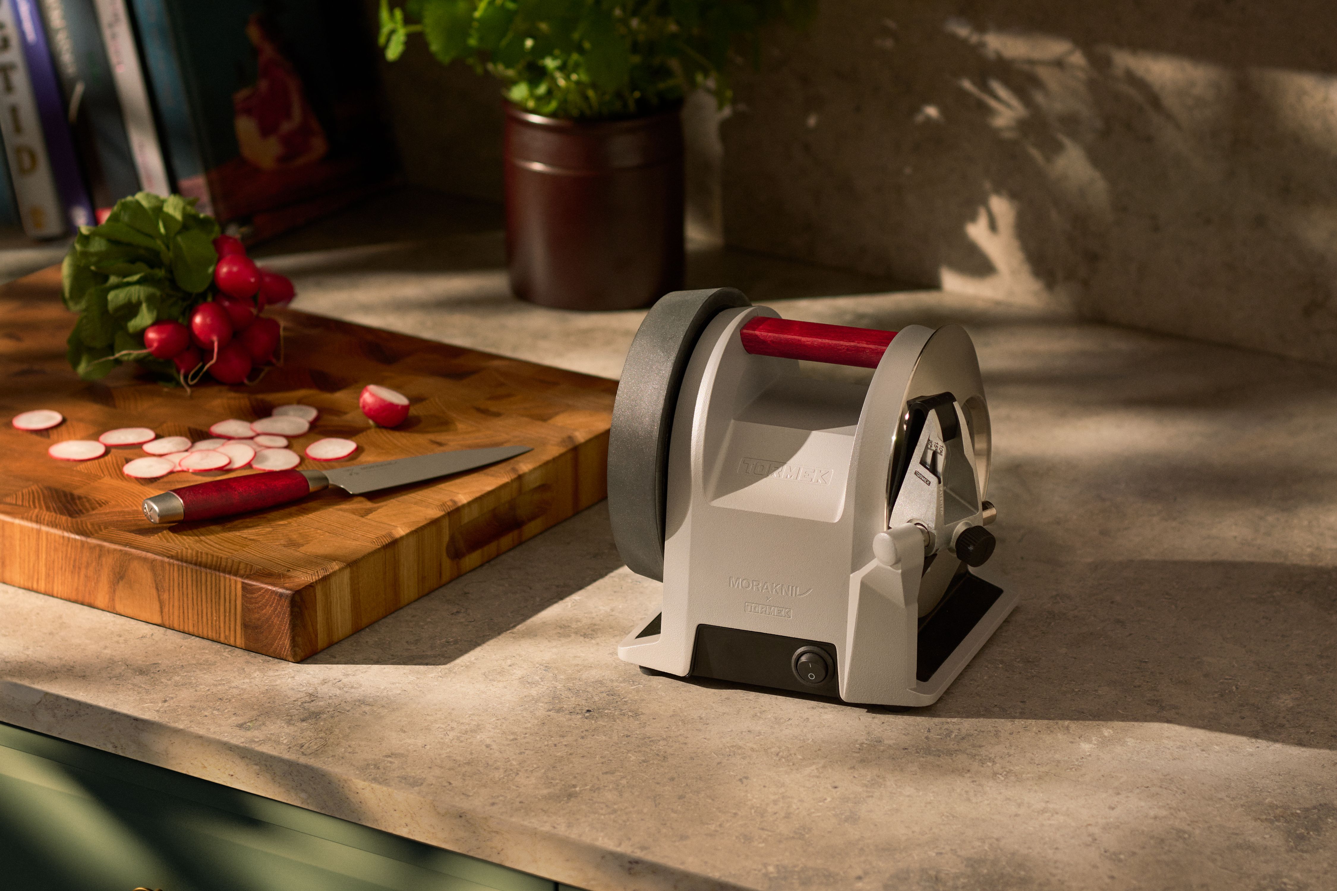 En grå och röd knivslip på en köksbänk bredvid en skärbräda med rädisor och en kniv.