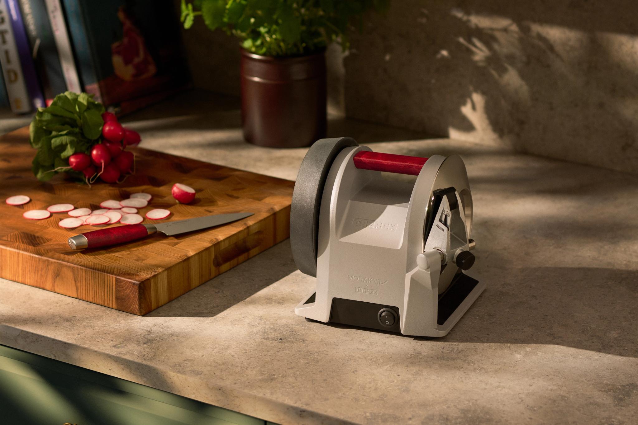 En grå och röd knivslip på en köksbänk bredvid en skärbräda med rädisor och en kniv.