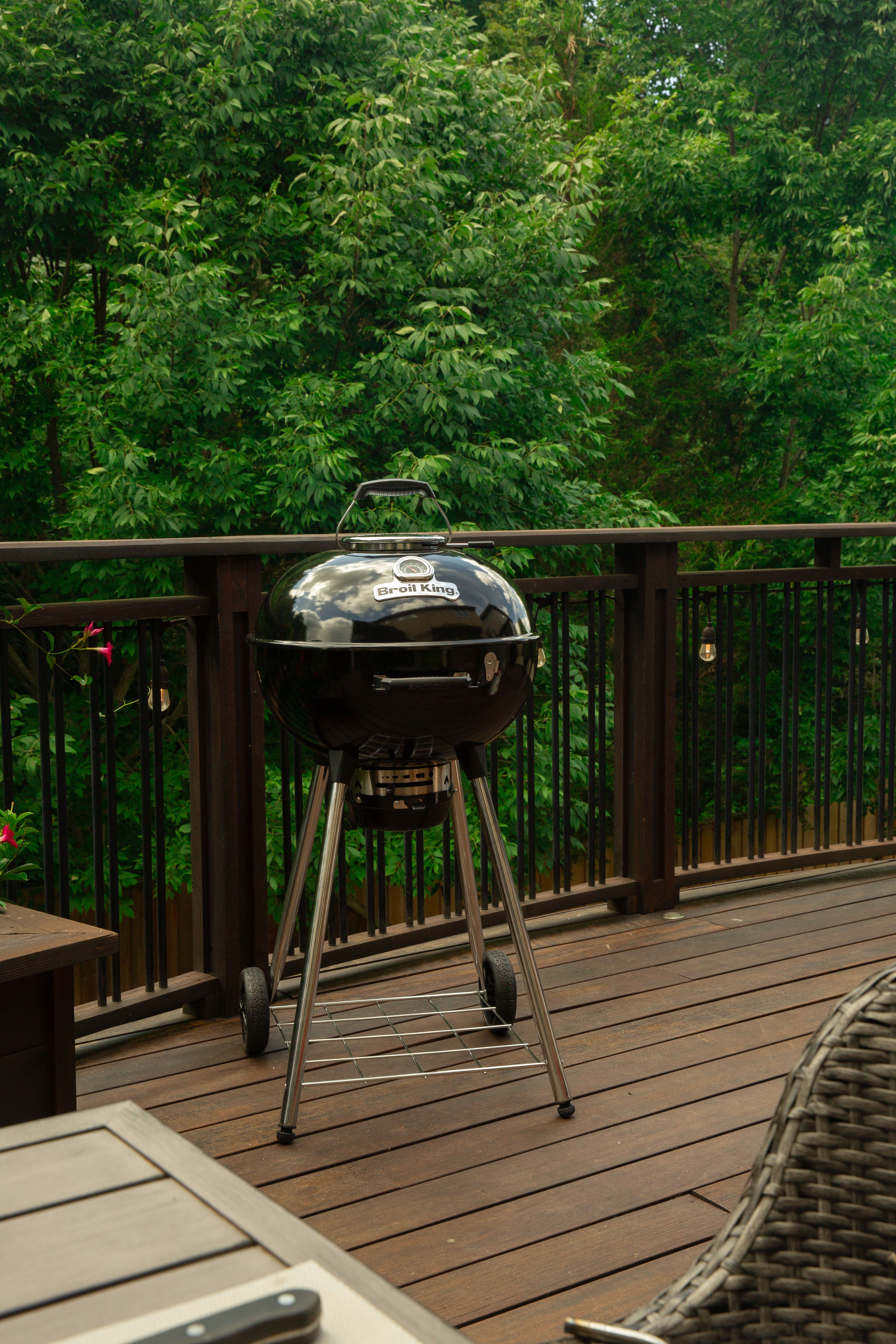 En svart kolgrill från Broil King står på en träaltan med gröna träd i bakgrunden