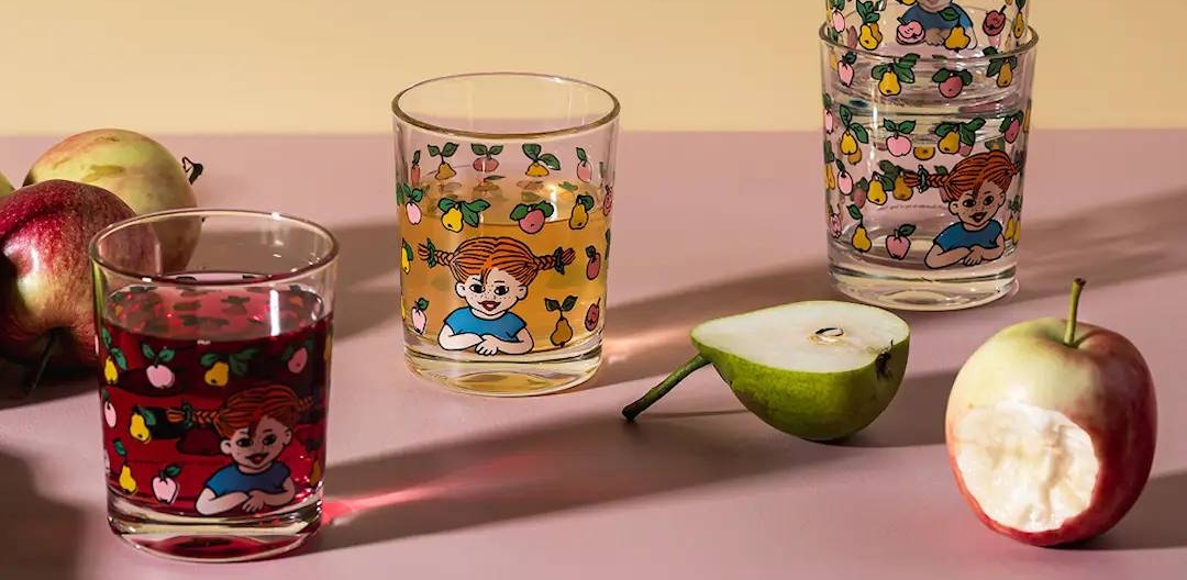 Neljä muurla lasia, jossa peppi kuviot, pureskeltu omena, puolikas päärynä ja kokonaisia omenoita pinkillä alustalla